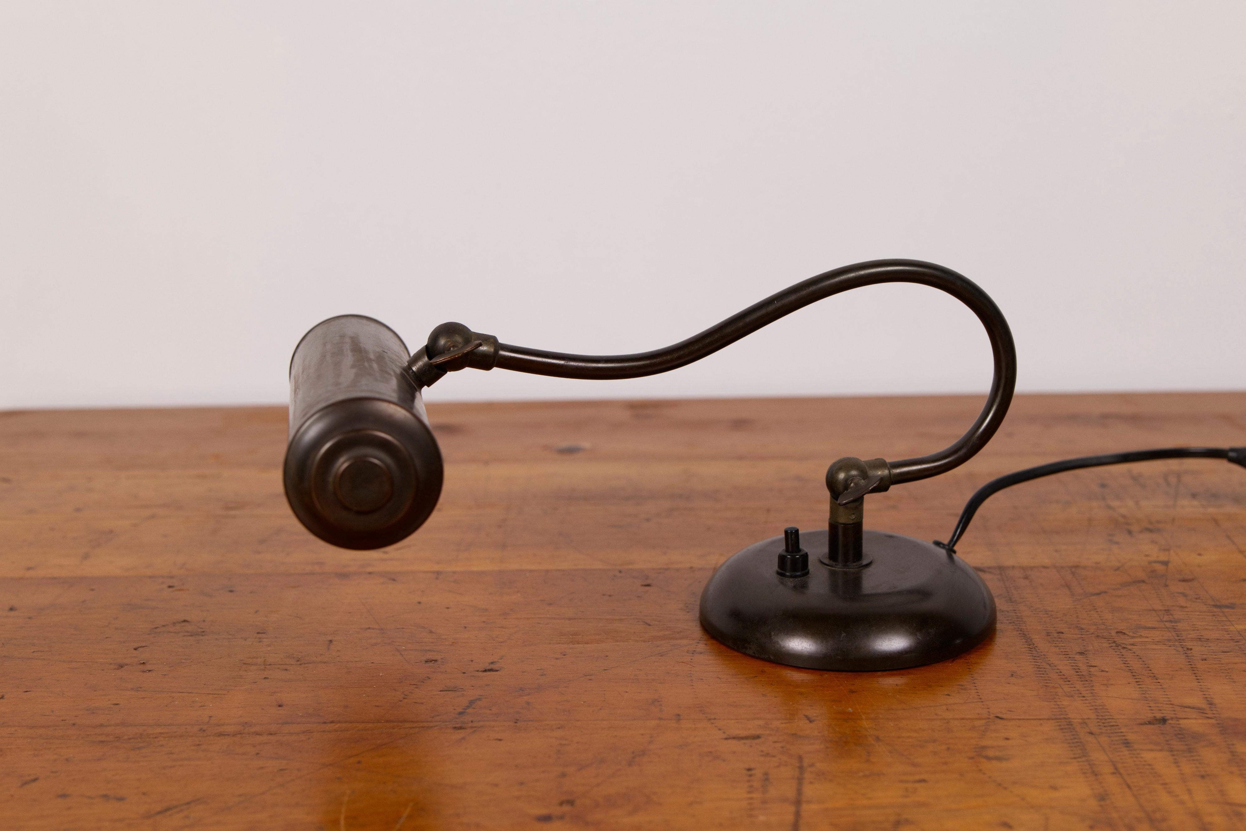 Eine raffinierte dänische Art-Déco-Klavier- oder Schreibtischlampe aus den 1930er Jahren, die skulpturale Eleganz mit funktionalem Charme verbindet. Die Leuchte verfügt über einen schlanken, geschwungenen Messingarm, der einen zylindrischen