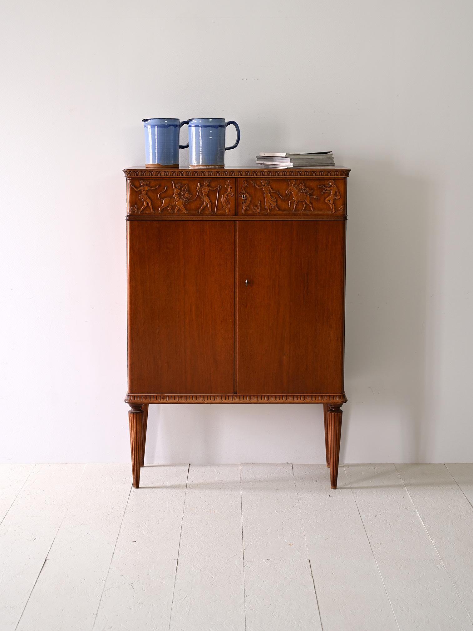 Scandinavian Art Deco cabinet with wood-carved bas-reliefs.

Original cabinet from the 1940s. The bas-relief depicting bucolic figures conceals four drawers. The lower part consists of a compartment with two shelves closed by two lockable hinged