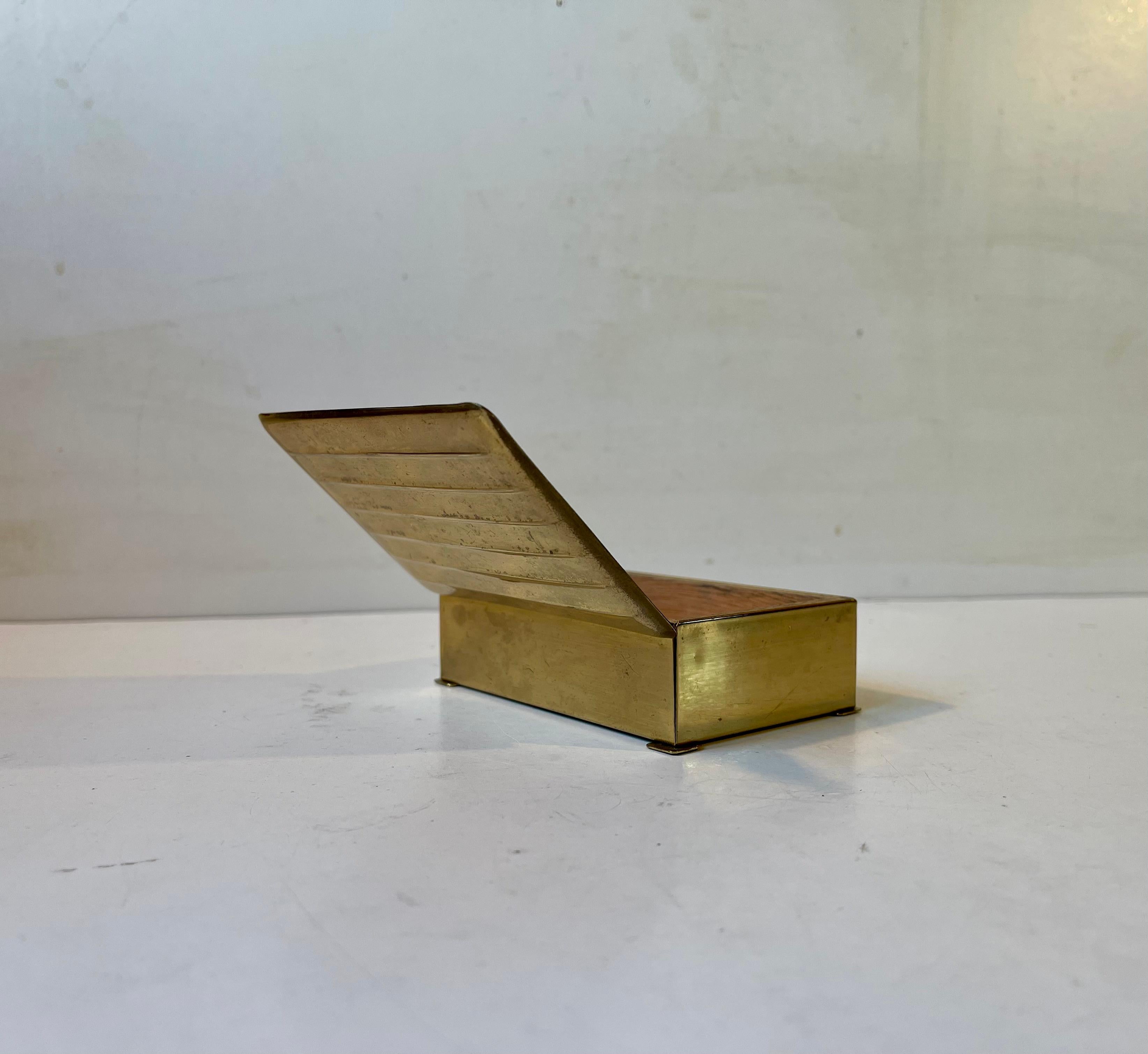 A brass cigarette or cigar box decorated horizontal ribbings/lines. It was made by an anonymous craftsman/designer in Scandinavia during the 1930s. It features a wooden lining that protects your tobacco. Measurements: W: 10 cm, Dept: 6.5 cm, Height