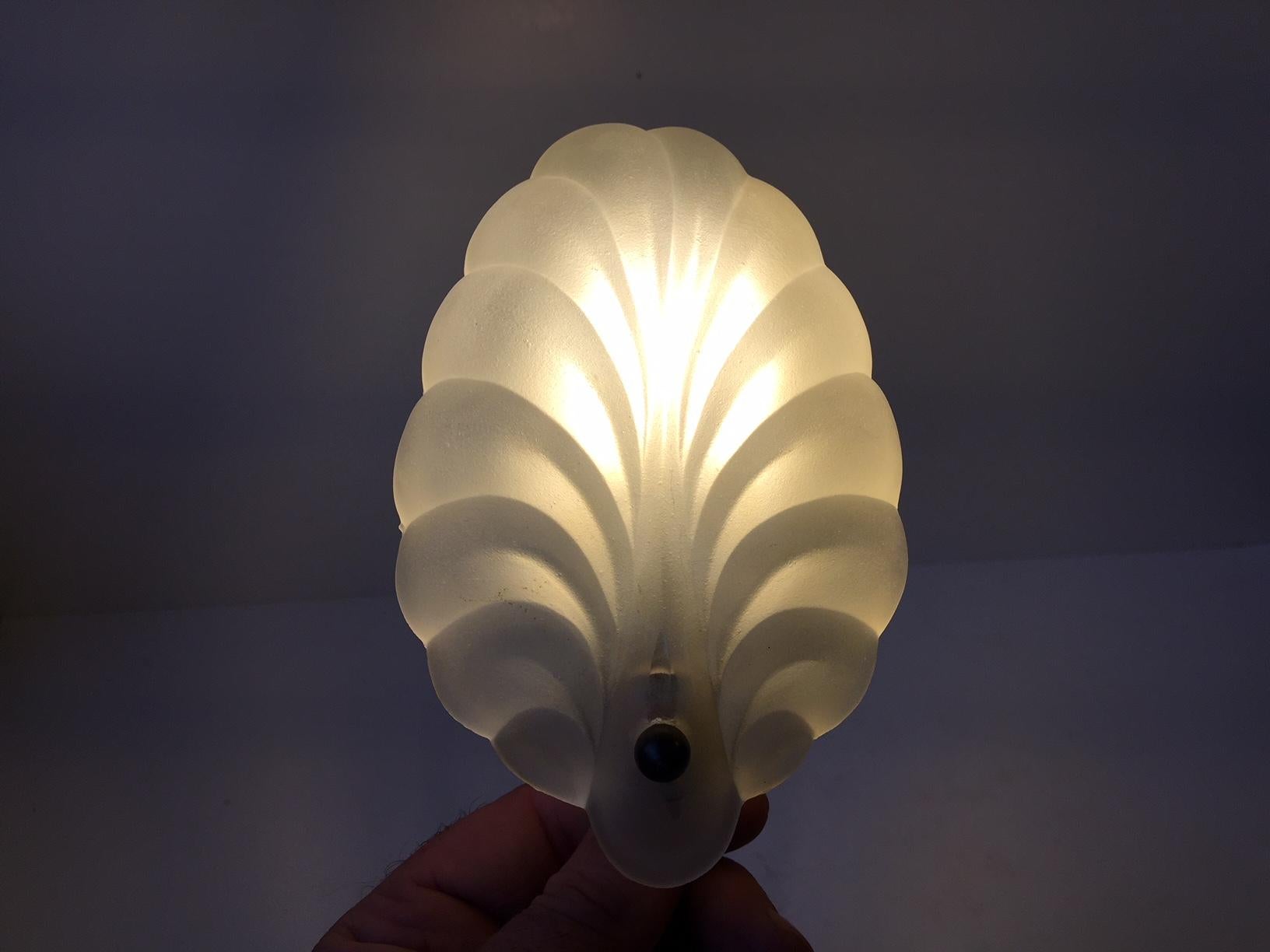 Small decorative wall light in frosted glass in the shape of a shell. Held in place to the mount by a patinated brass ball. It was Manufactured in Scandinavia in the 1930s in a style reminiscent of C. T. Kalmar and Orrefors.