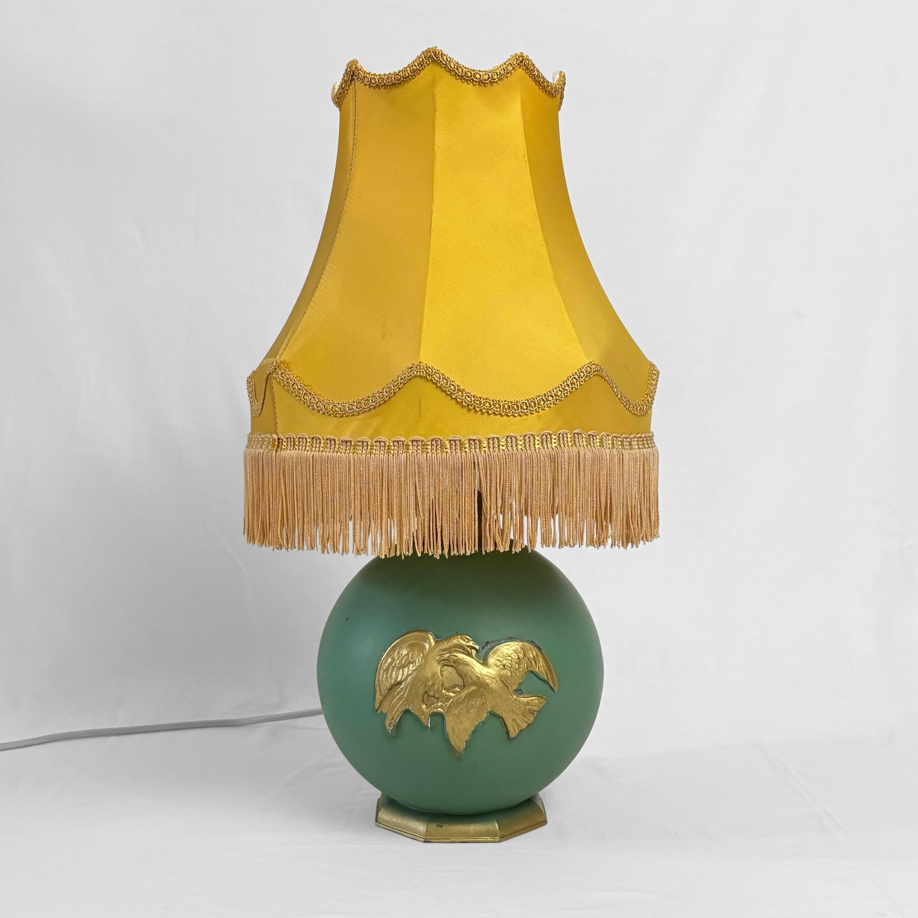 A beautiful Art Deco table lamp, crafted from metal with a globe-shaped base, a porcelain lamp holder with an integrated porcelain light switch, and a hexagonal foot. It is decorated with a dramatic scene depicting two birds of prey fighting.