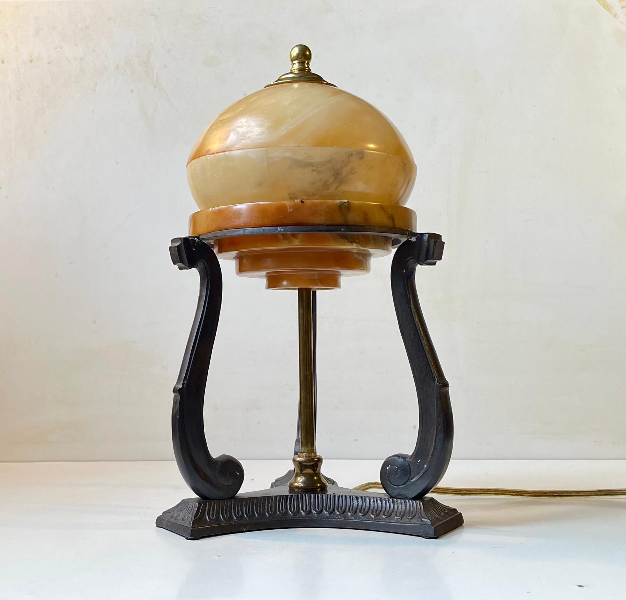 Interesting table light inspired by architectural art deco elements. It features an alabaster shade freely resting on a bronze tri-stand. This light was anonymously made in Scandinavia during the 1930s or 40s. It's in working order. 

Measurements: