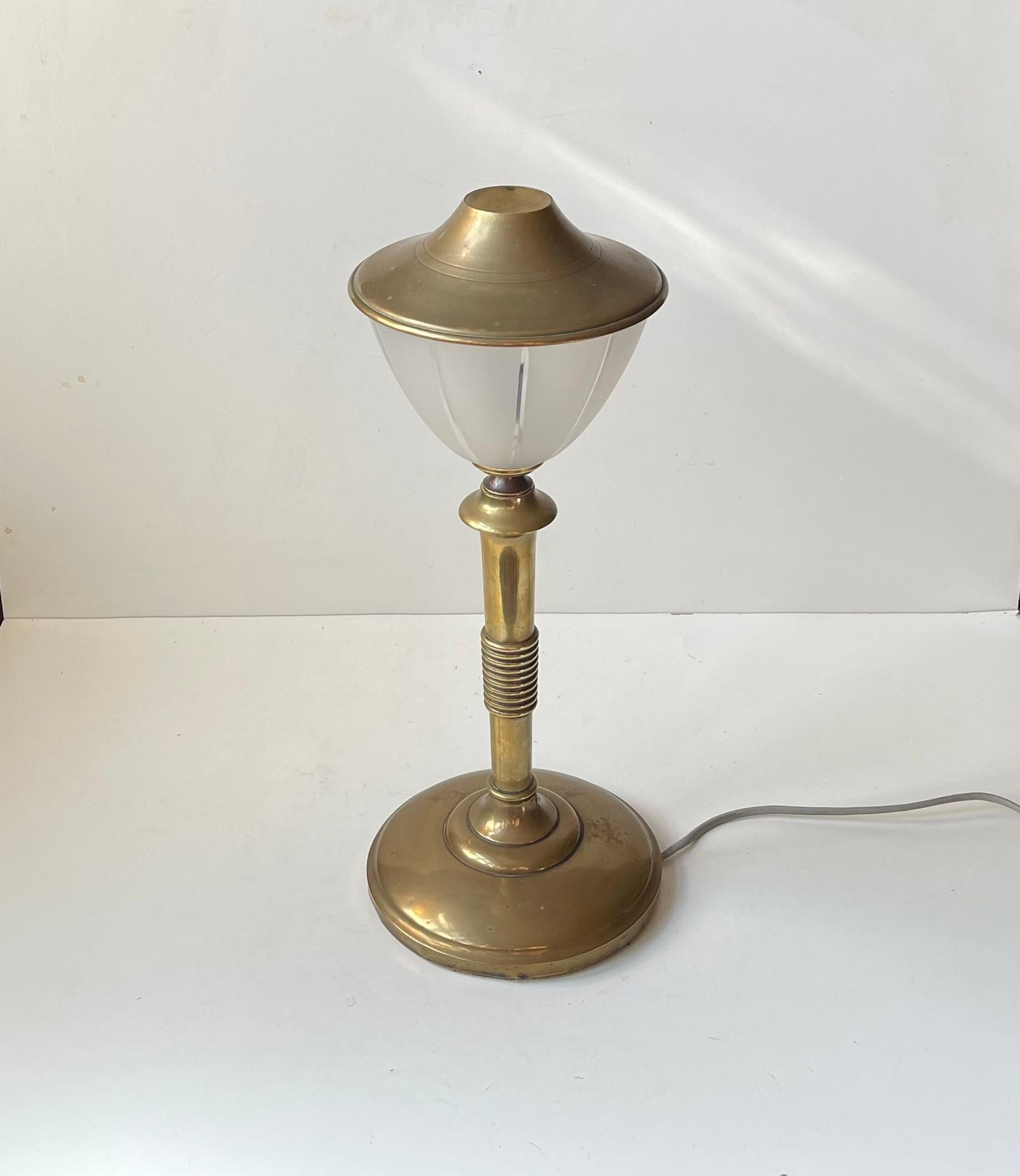 Art Deco style table lamp made in Scandinavia during the 1930s or 40s. It features an architecturally perceived bronze base and rod with stylish center rings, a vertically striped cut frosted glass shade upon which a patinated solid brass shade is