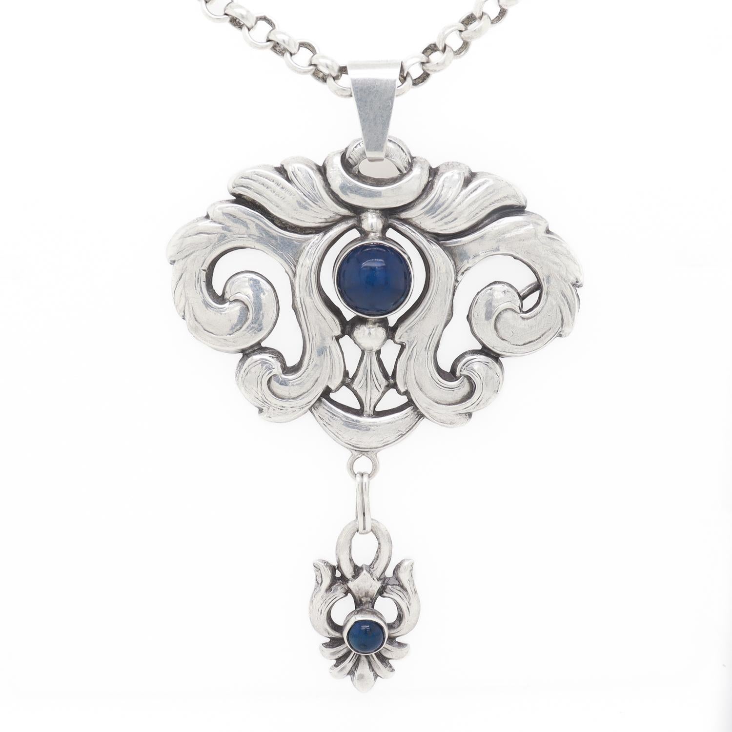 Una raffinata collana con ciondolo in argento Art Nouveau.

Nello stile di William Fuglede di Copenhagen.

Probabilmente convertito da spilla a ciondolo.

Il ciondolo e la goccia sono caratterizzati da elementi a spirale e cabochon di lapis