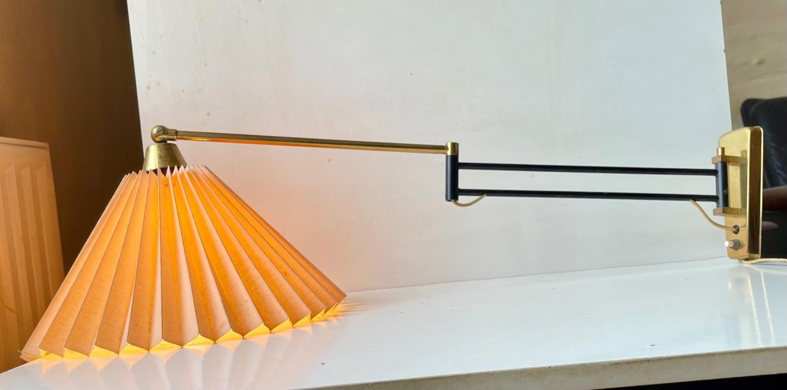 Dept/reach adjustable wall sconce made from brass - partially lacquered in black. Made in Scandinavia during the 1960s in a style reminiscent of Svend Aage Holm Sørensen. It features a fluted Danish textile shade (pastel/light brown) adjustable at