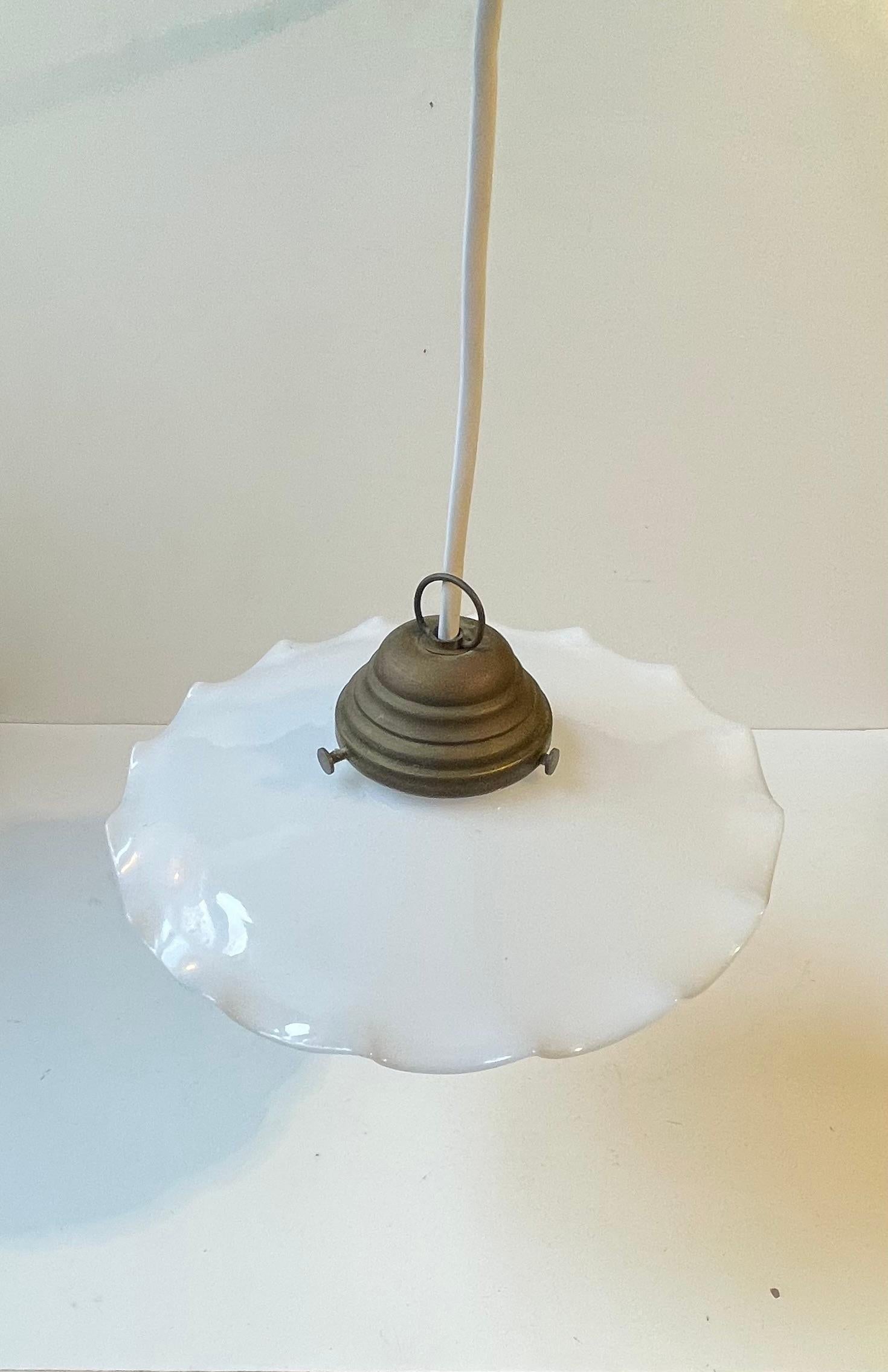 Una lampada a sospensione Ballerina, semplice e felina, realizzata in ottone patinato e dotata di un paralume in vetro opalino sfumato, probabilmente prodotto da Holmegaard in Danimarca intorno al 1920-30. Viene fornito in condizioni originali con