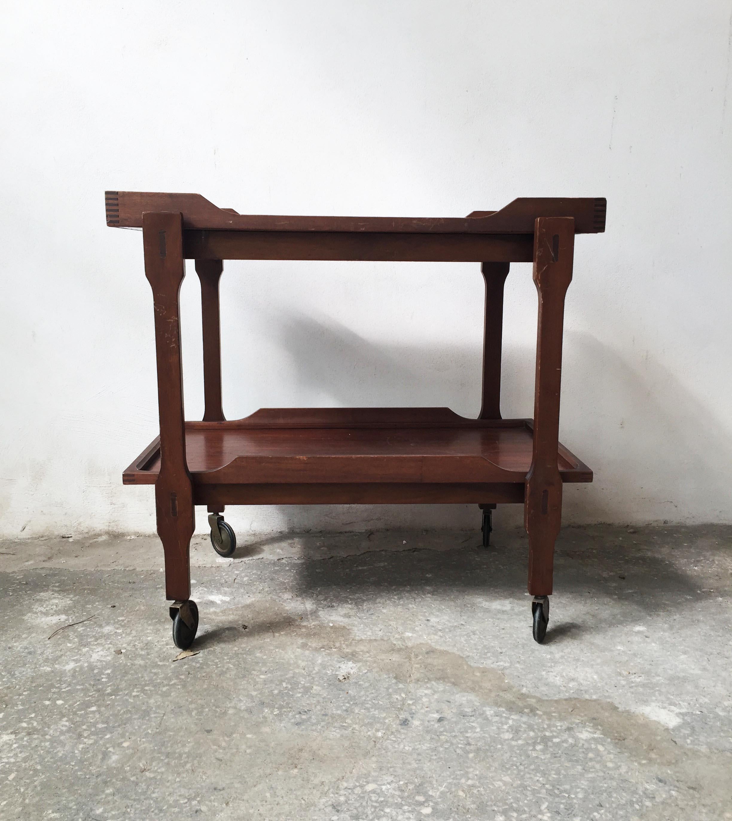 Geometrical and pure lines characterized this Scandinavian bar cart in teak wood.
The upper tray is removable and present two recess handles while the lower is fixed (without handles).
Both of trays are in mahogany wood and the four wheels are in