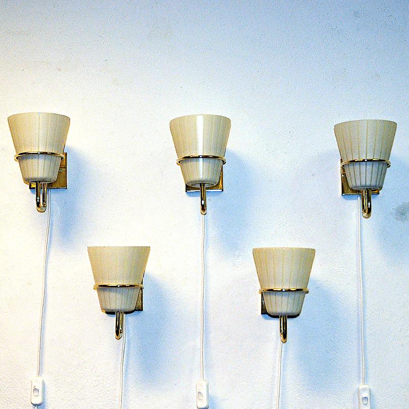 Applique scandinave en laiton et verre opalin du milieu du siècle dernier, datant des années 1950. Chaque lampe est maintenue par une plaque arrière en laiton et un support en laiton pour l'abat-jour amovible en verre opalin en forme de cône.