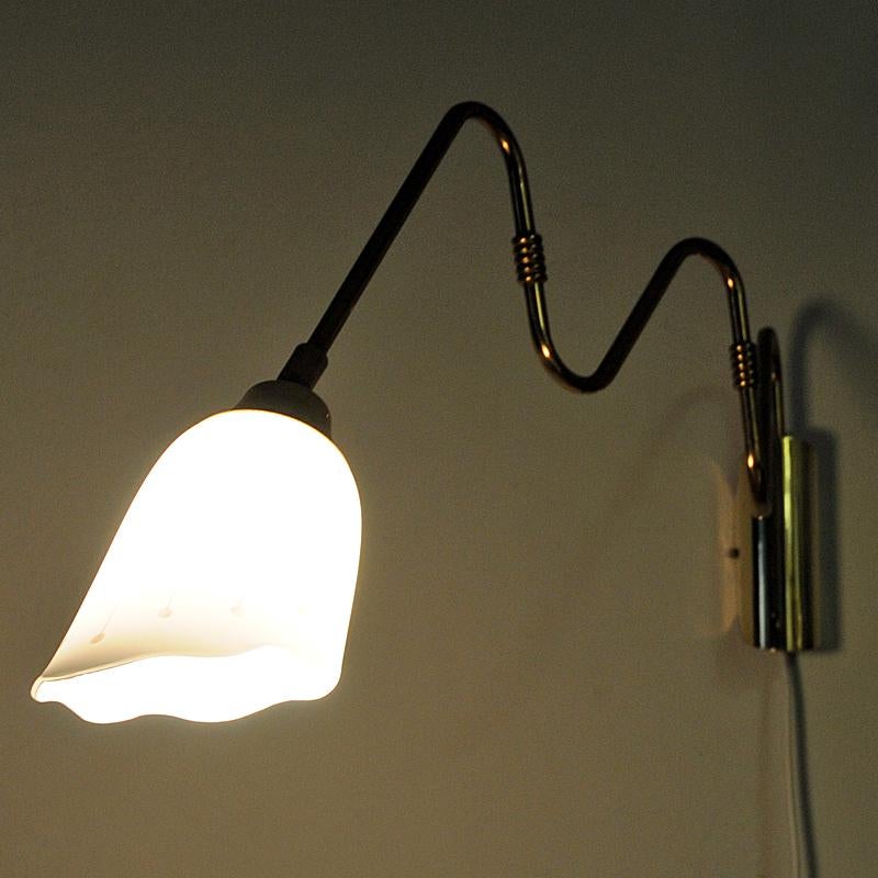 Lovely and adjustable Scandinavian brass wall lamp with a flower shaped white glass shade - from the 1950s. The brass arm is adjustable to the right and left, in and out. Polished brass. Gives a nice and calming light when lit. Marked SSL. Measures: