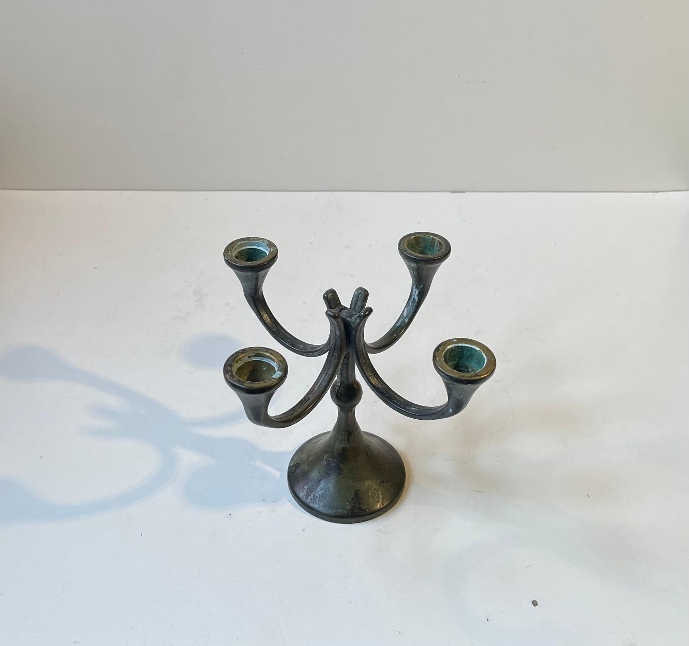 A small scaled ( H: 14.5, W/D: 19 cm) candelabrum for 4 regular sized candles. It is fashioned from patinated bronze and showcases distinct Neo-gothic/brutalist vibes. It was possibly made by Ystad/Scandia Presents in Sweden during the 1970s. It has