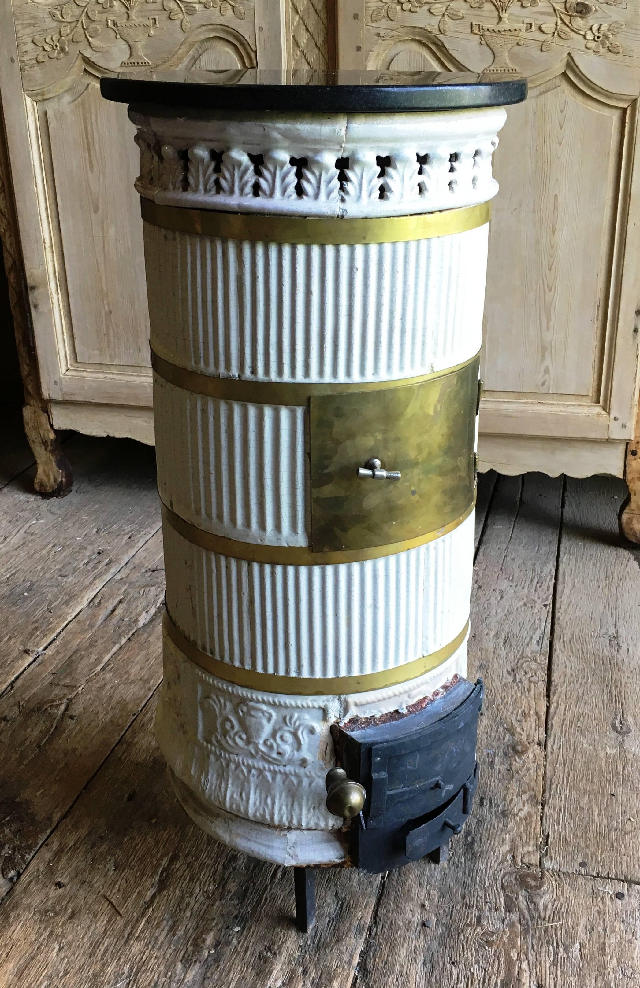 A charming Scandinavian white ceramic parlor stove with a black stone top and iron and brass doors, Gustavian style.