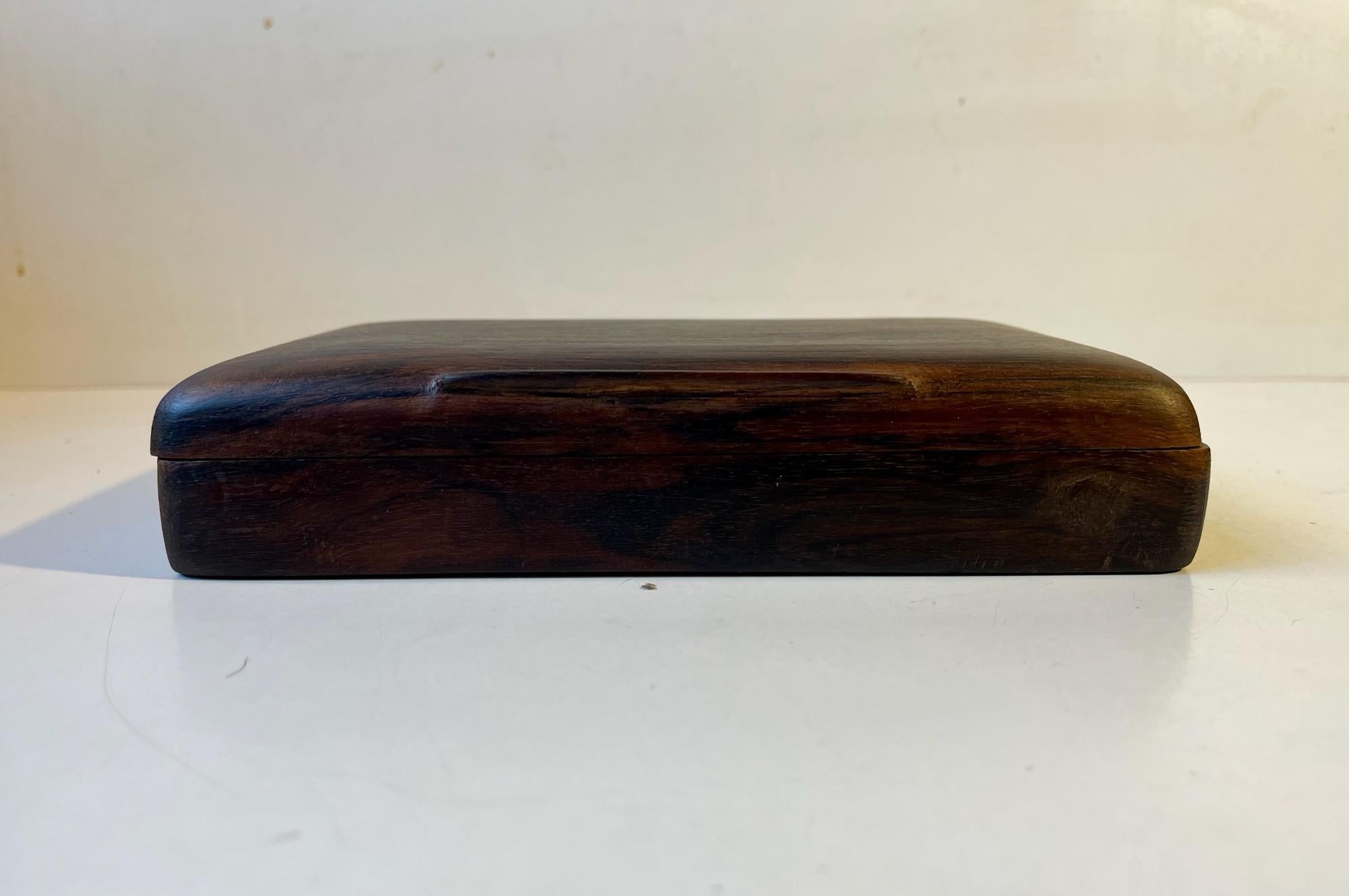 A handmade box for cigarettes and /or cigars. Its made from solid rosewood and displays beautiful craftsmanship with its rounded of edges and particularly to the carved and lid-opener. It features two square compartments. Measurements: 20 x 13 x 4