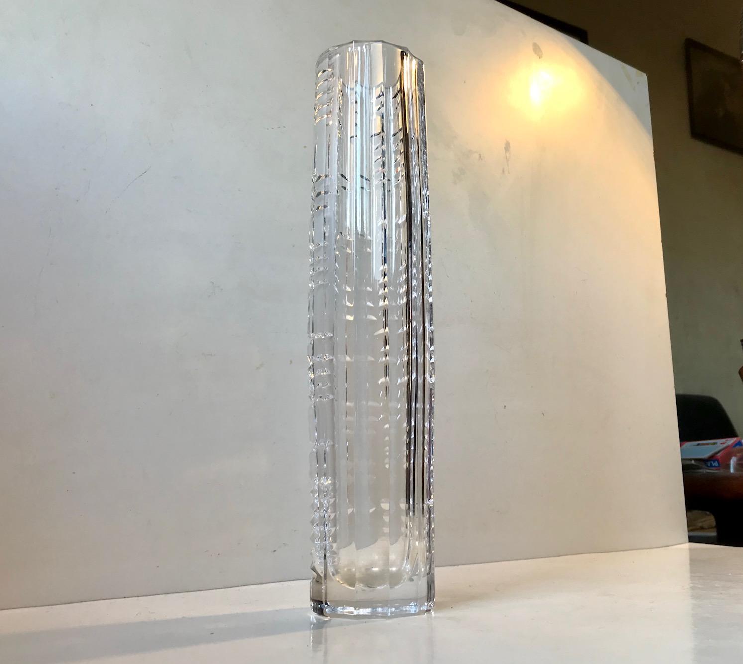 A cut crystal torpedo shaped vase presumably from either Kosta Boda or Orrefors. The vase features diffrent techniques most prominent is the mix of vertical ribbing to one side and a geometric crisscross of arrow patterns top the other side. It