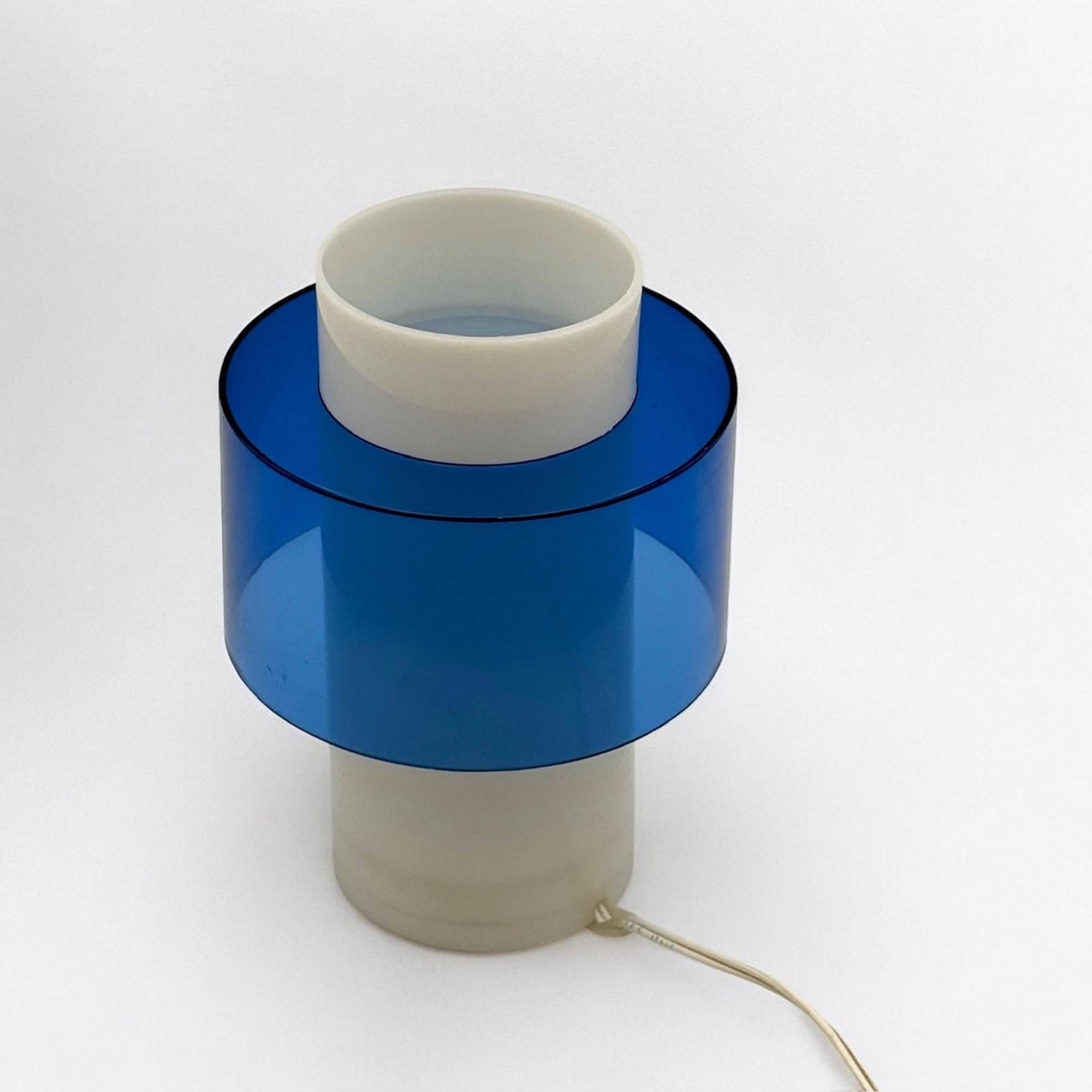 Un hommage éclatant au style nordique minimaliste : cette lampe scandinave des années 70 capture l'essence d'un design épuré et d'une lumière atmosphérique. La structure combine un cylindre en acrylique blanc mat avec un insert bleu translucide