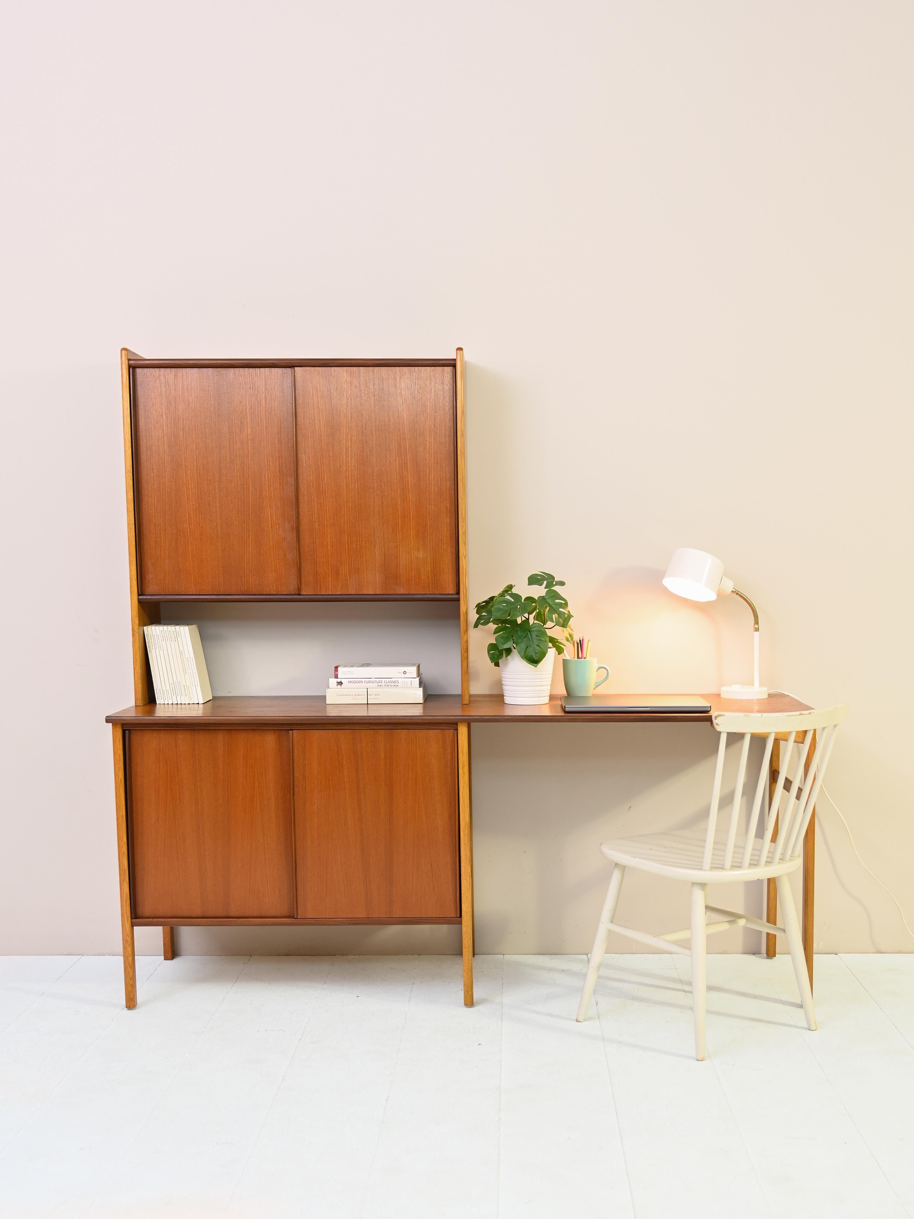 Particular mid-century teak desk with storage compartment and bookcase.

The regular structure features a storage compartment with sliding doors on one side and two slender, tapered legs on the other. 
A large bookcase rests on the desk
