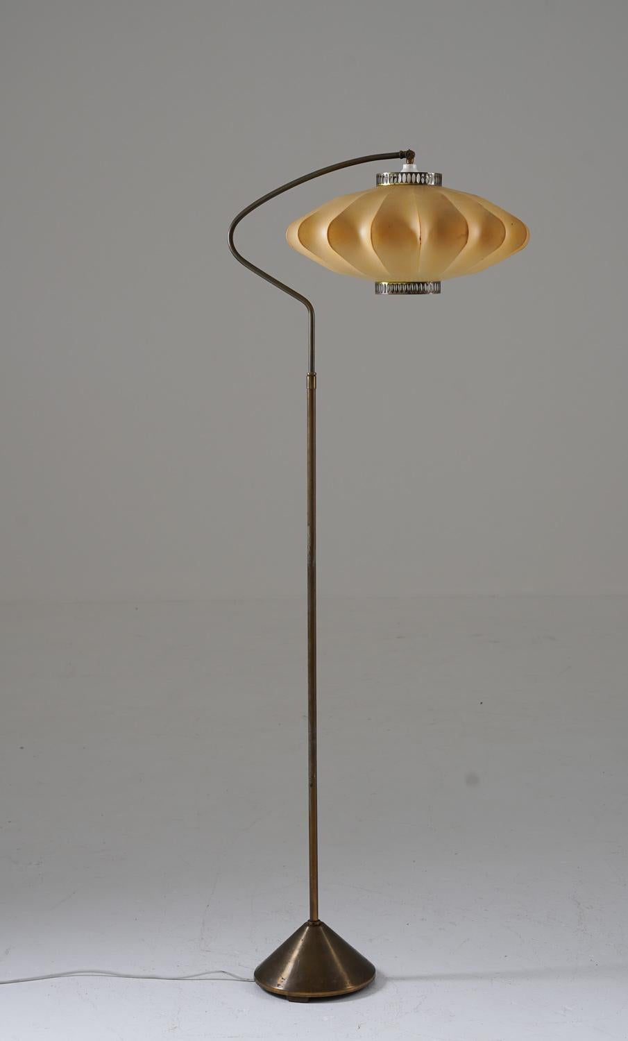 Beautiful floor lamp manufactured in Denmark, 1950s.
This floor lamp consists of a beautifully curved brass rod, supported by a cone-shaped base. The light source is hidden by a large cocoon shade with perforated brass details.

Condition: Good