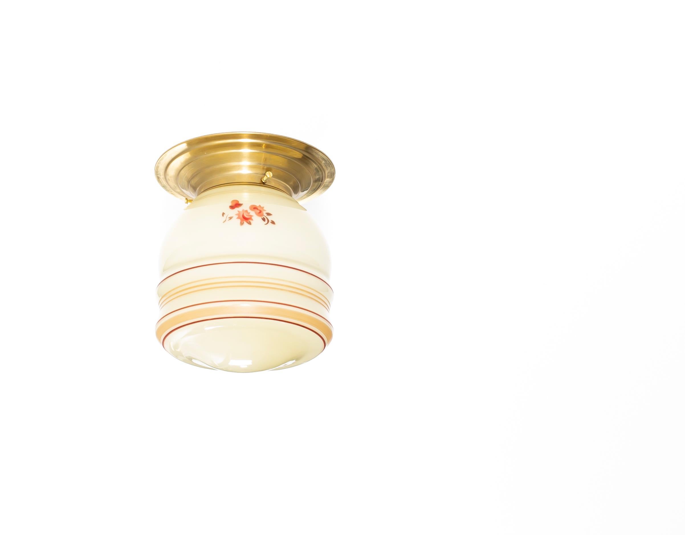 Splendido e decorativo apparecchio da soffitto a incasso della prima metà degli anni '50. La plafoniera ha un paralume in vetro color crema con motivi floreali dipinti a mano nei toni caldi del rosso e sottili bande lineari in rosso e ocra, che