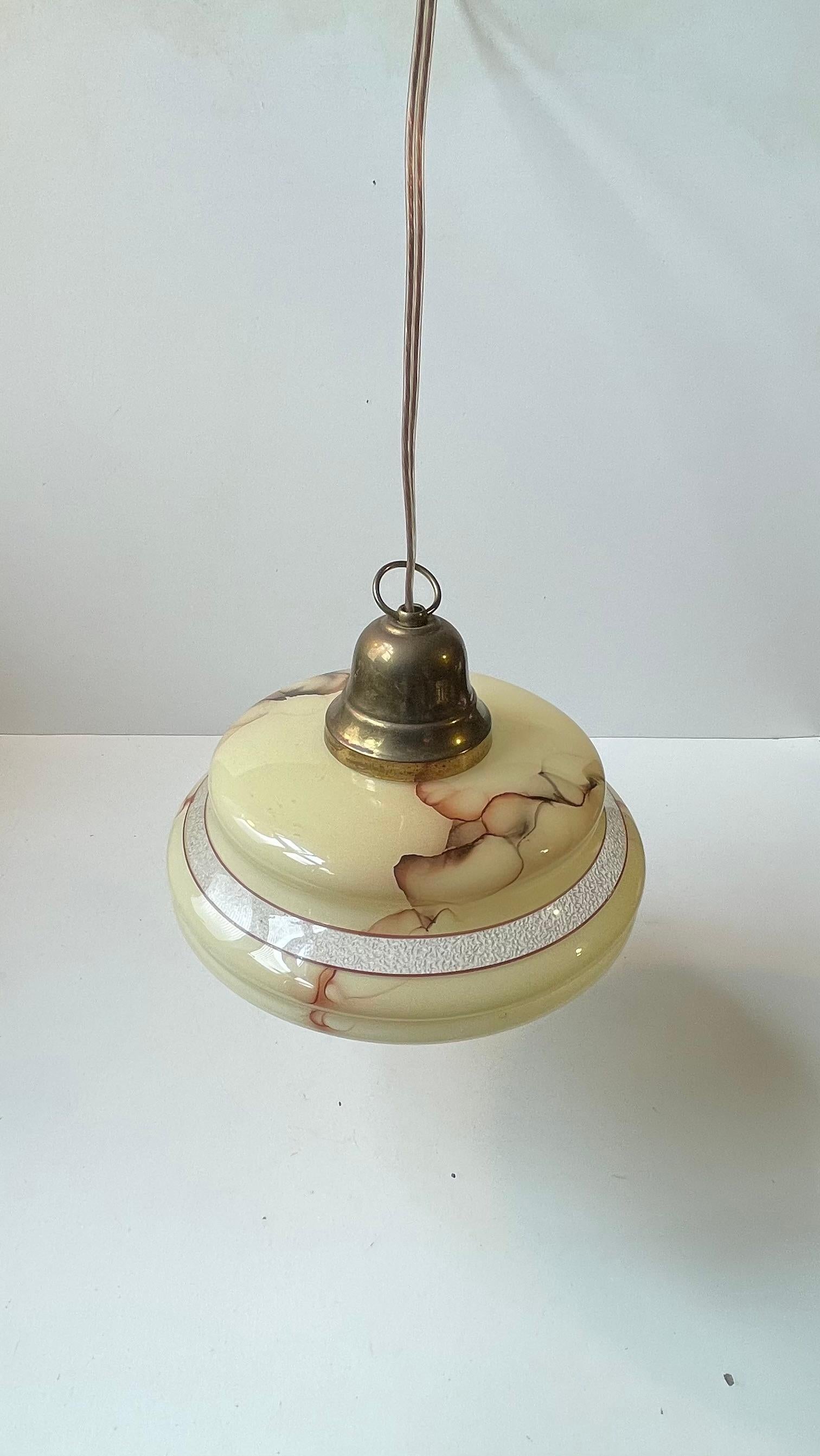 Piccola lampada a sospensione composta da un paralume in vetro opalino color crema pastello decorato con effetti di marmo. Presenta un piano in ottone massiccio patinato con un anello. Fu prodotto in Scandinavia negli anni '40. Lo stile
