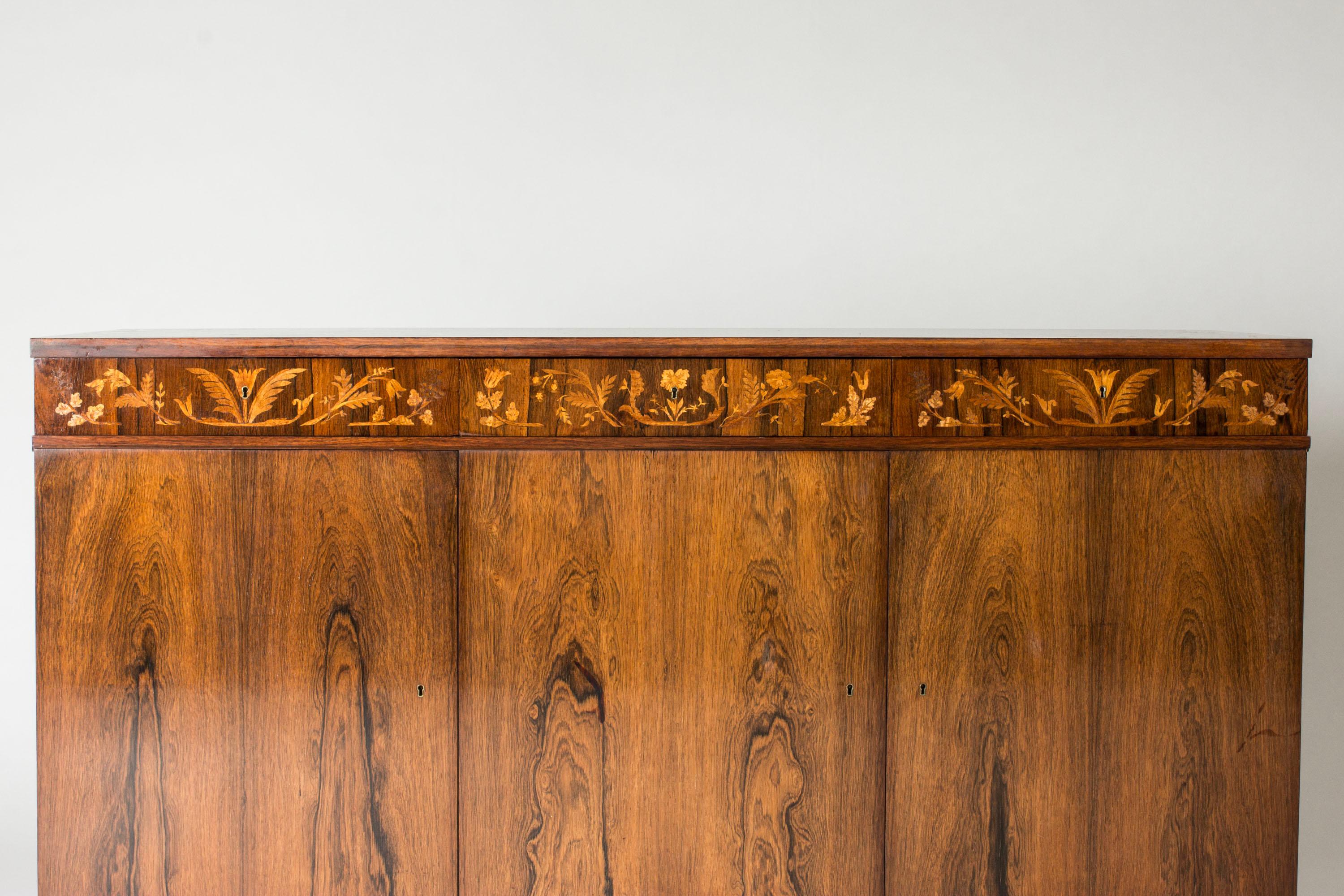 Precioso aparador de Carl Malmsten, con elegante chapado de palisandro, decorado en el borde y la parte superior con incrustaciones de flores y hojas en una madera más clara. Pies gruesos con líneas diagonales.
