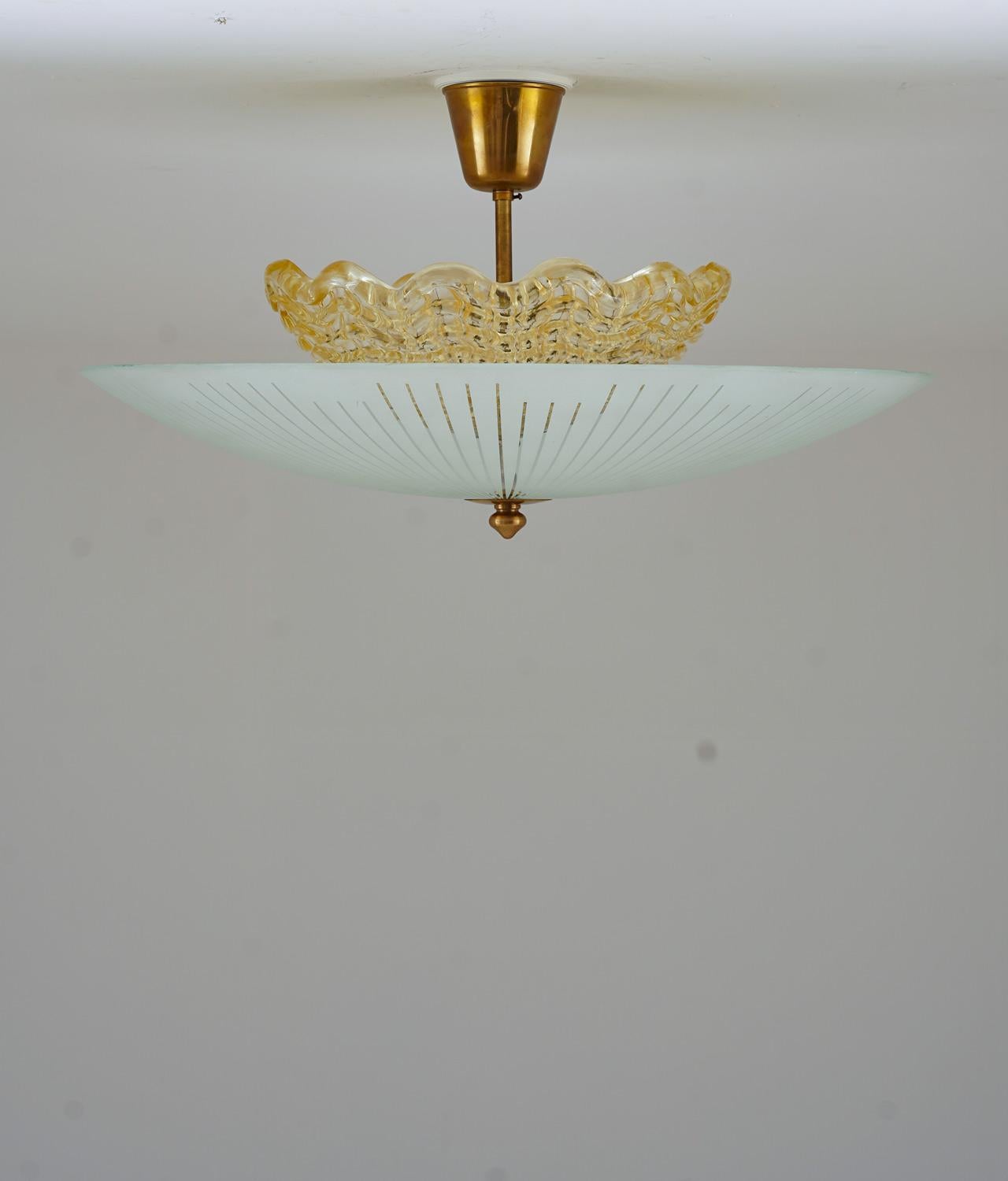 Beautiful flush mount in brass and frosted glass, produced by Orrefors in Sweden circa 1950.
The lamp consists of an amber-colored inner shade, hiding three light bulbs. The inne shade is surrounded by a large outer shade in frosted glass.