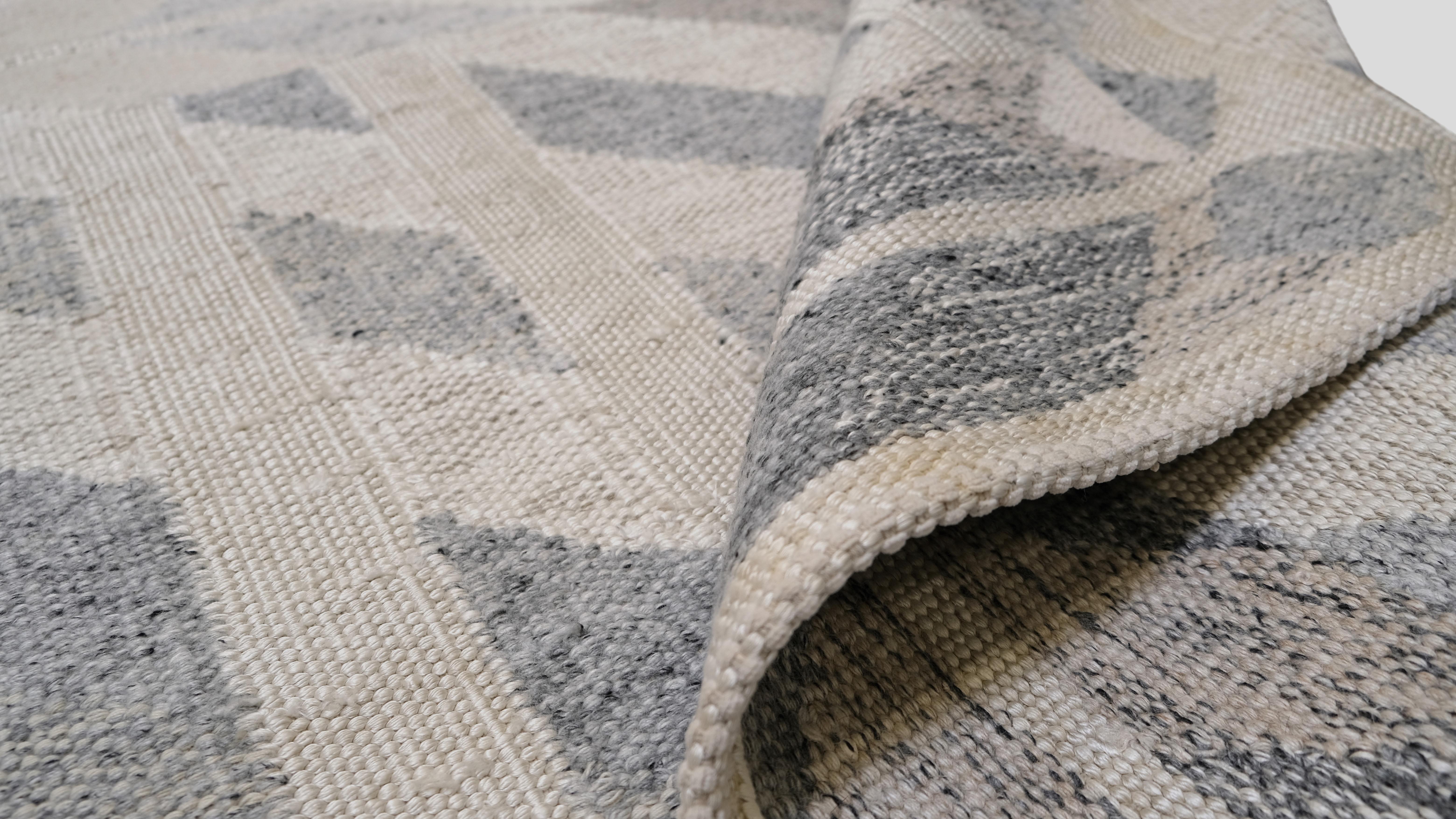Bringen Sie zeitgenössische Eleganz in Ihren Raum mit diesem modernen geometrischen  Teppich aus Wollgemisch. Dieser Teppich mit seinem auffälligen, symmetrischen, kantigen Muster ist in einer raffinierten Palette von Grau- und Elfenbeintönen