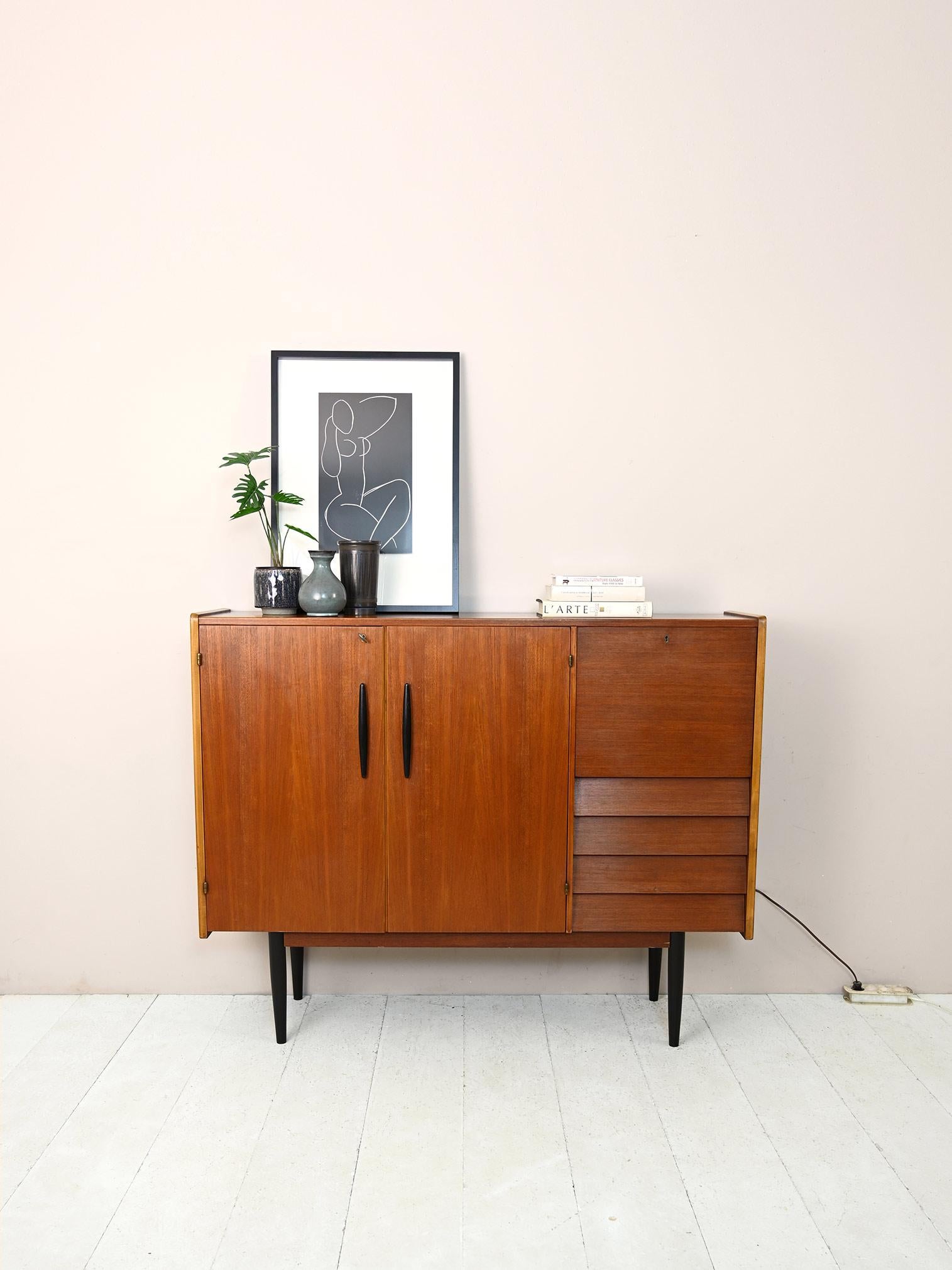1960s teak sideboard with backlit storage compartment.

A modern piece of furniture with a retro feel consisting of a large storage compartment with hinged doors, 4 drawers and a flap.
It features black-painted details found in the wooden door