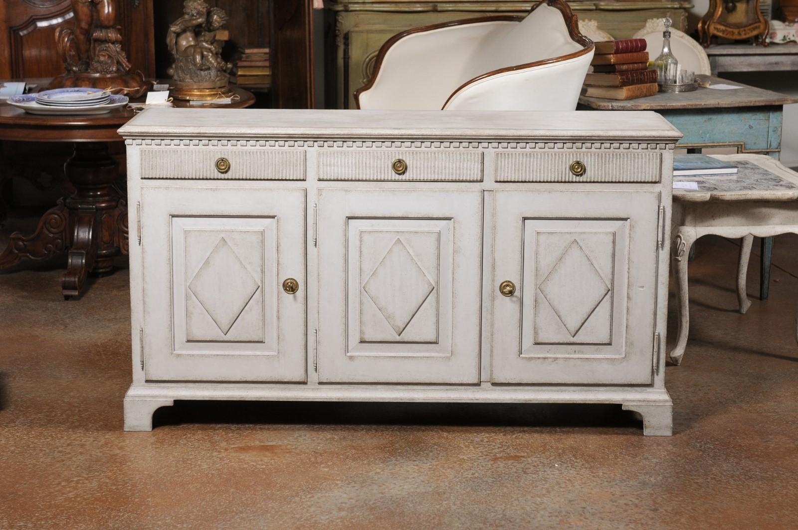 A Scandinavian late Gustavian style painted wood sideboard from the 20th century, with three drawers over three doors and diamond motifs. Created in Scandinavia during the 20th century, this sideboard features a rectangular top sitting above a
