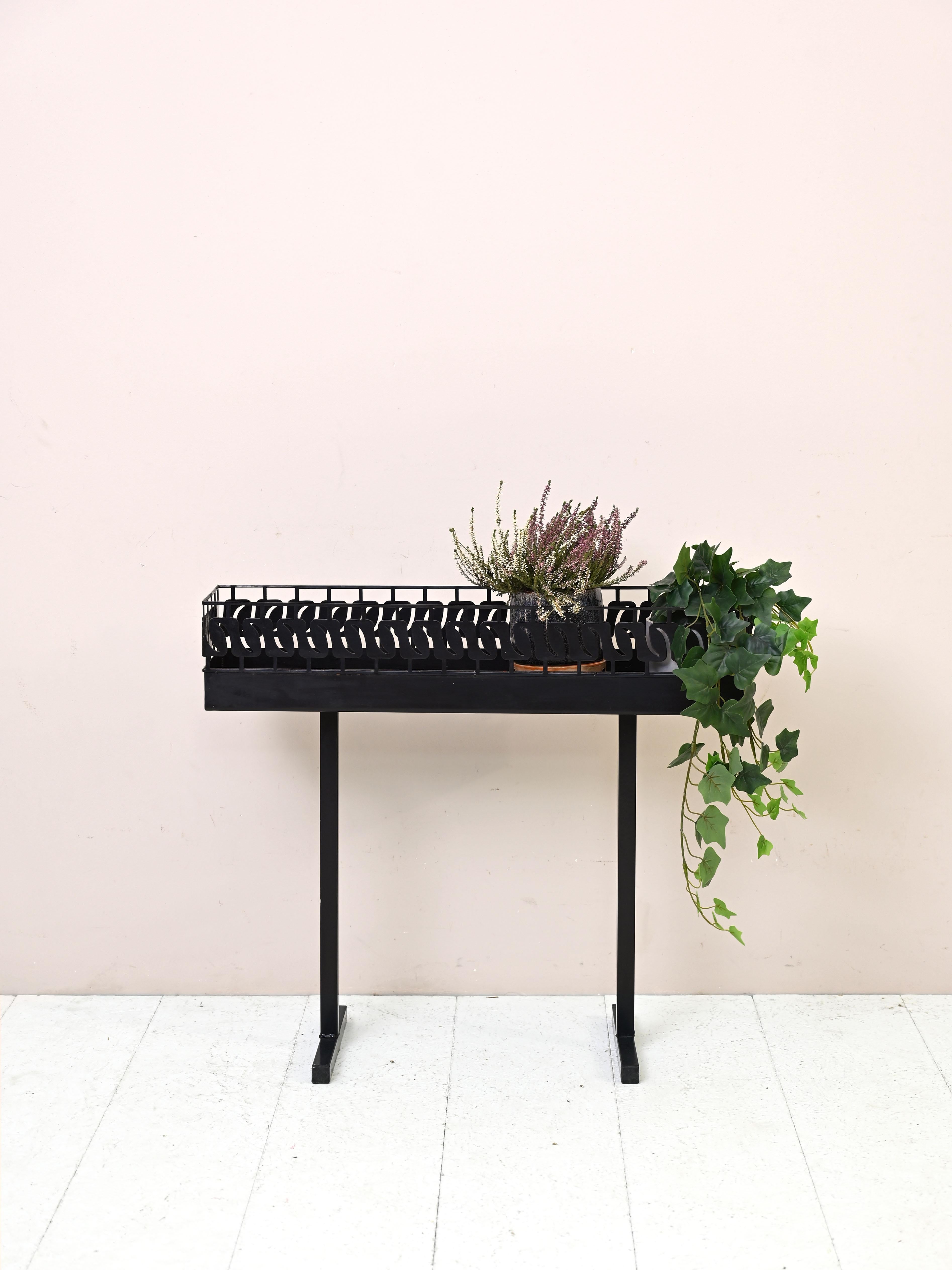 Portafiori vintage da interno/esterno.

Realizzata in metallo verniciato nero, questa fioriera presenta due semplici supporti che fungono da gambe e una base con un bordo in metallo lavorato.

Buone condizioni vintage. Prestare attenzione alle