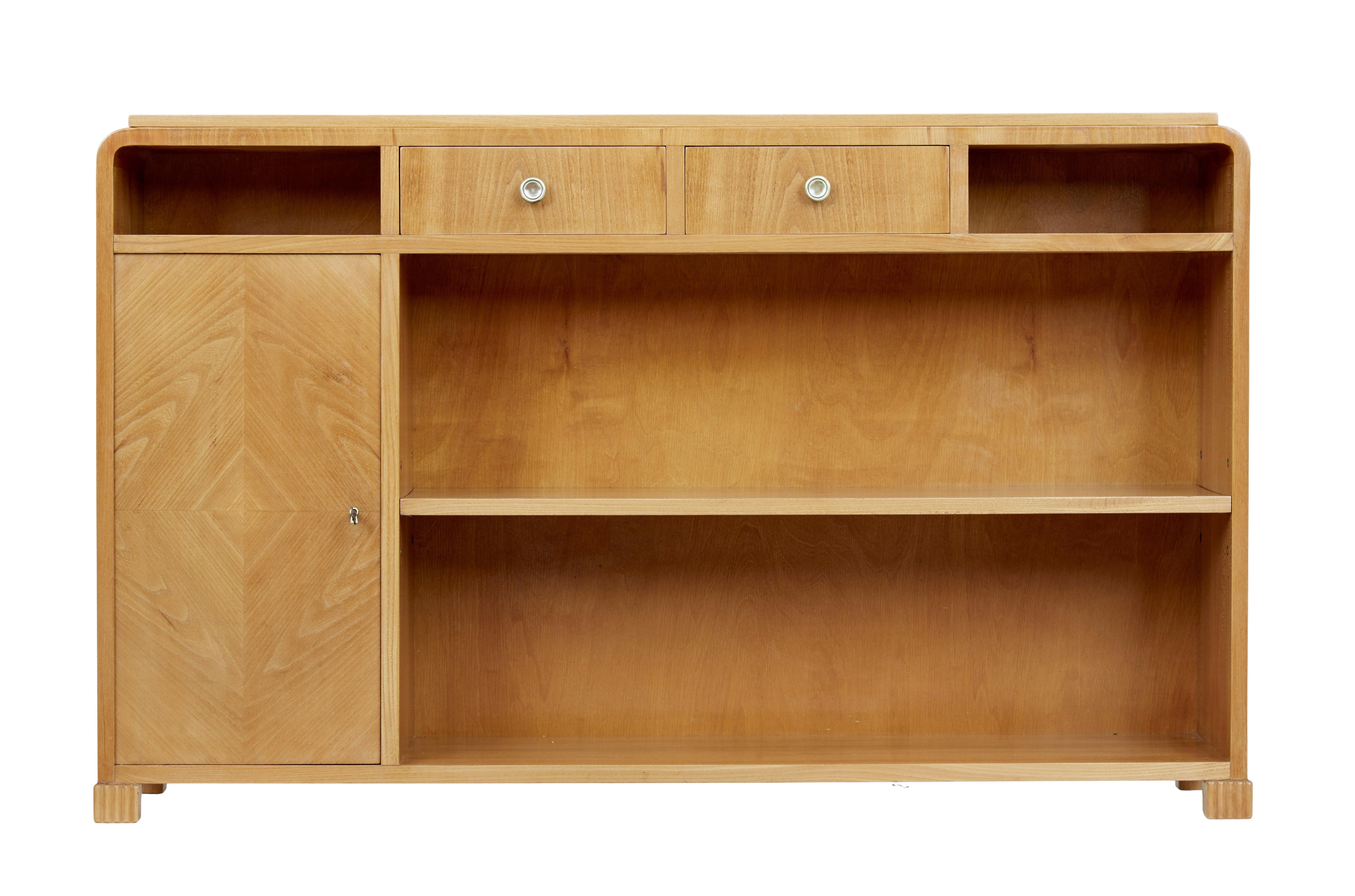 Scandinavian mid-20th century elm low bookcase, circa 1950.

Good quality Swedish elm bookcase with a cupboard. Art Deco inspired stepped top surface, below which are 2 drawers flanked either side with a pigeon holes for storage.

Main open