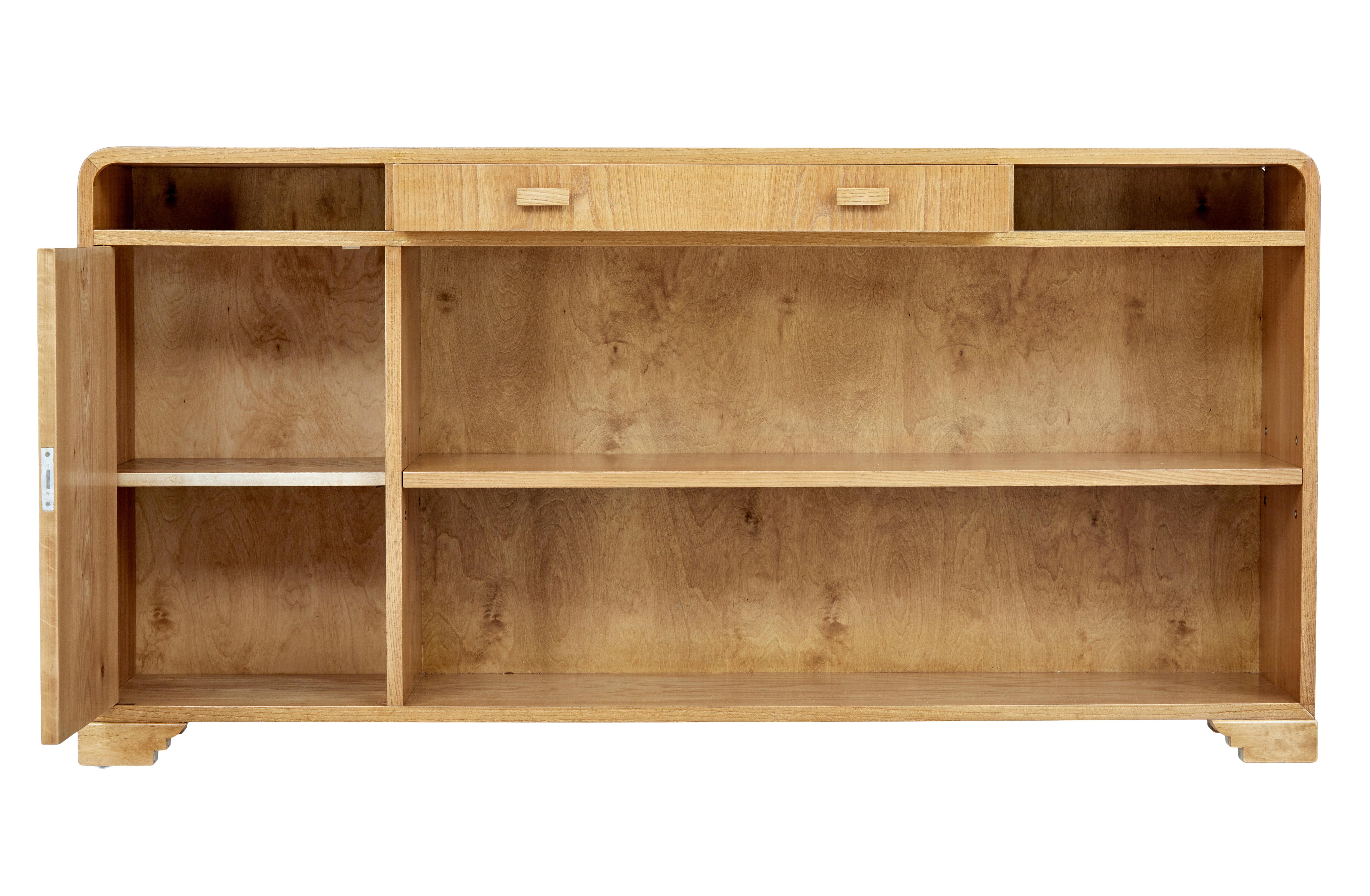 Scandinavian mid-20th century elm low open bookcase, circa 1950.

Superb storage solution for small spaces. Beautifully veneered in elm, with rounded corners to provide that deco inspired look. Central drawer below the top surface with an open