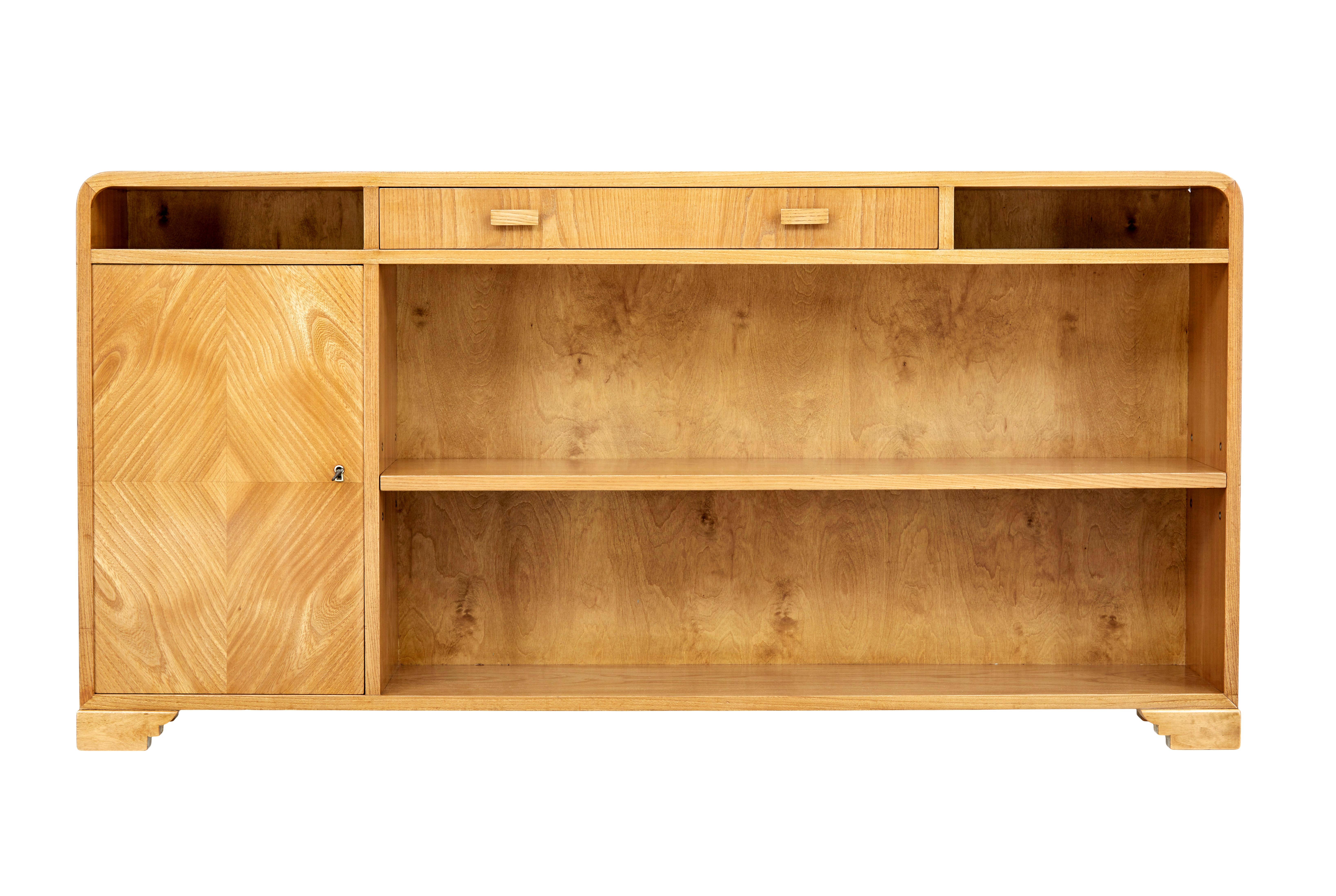 Scandinavian mid 20th century elm low open bookcase circa 1950.

Superb storage solution for small spaces.  Beautifully veneered in elm, with rounded corners to provide that deco inspired look.   Central drawer below the top surface with a open