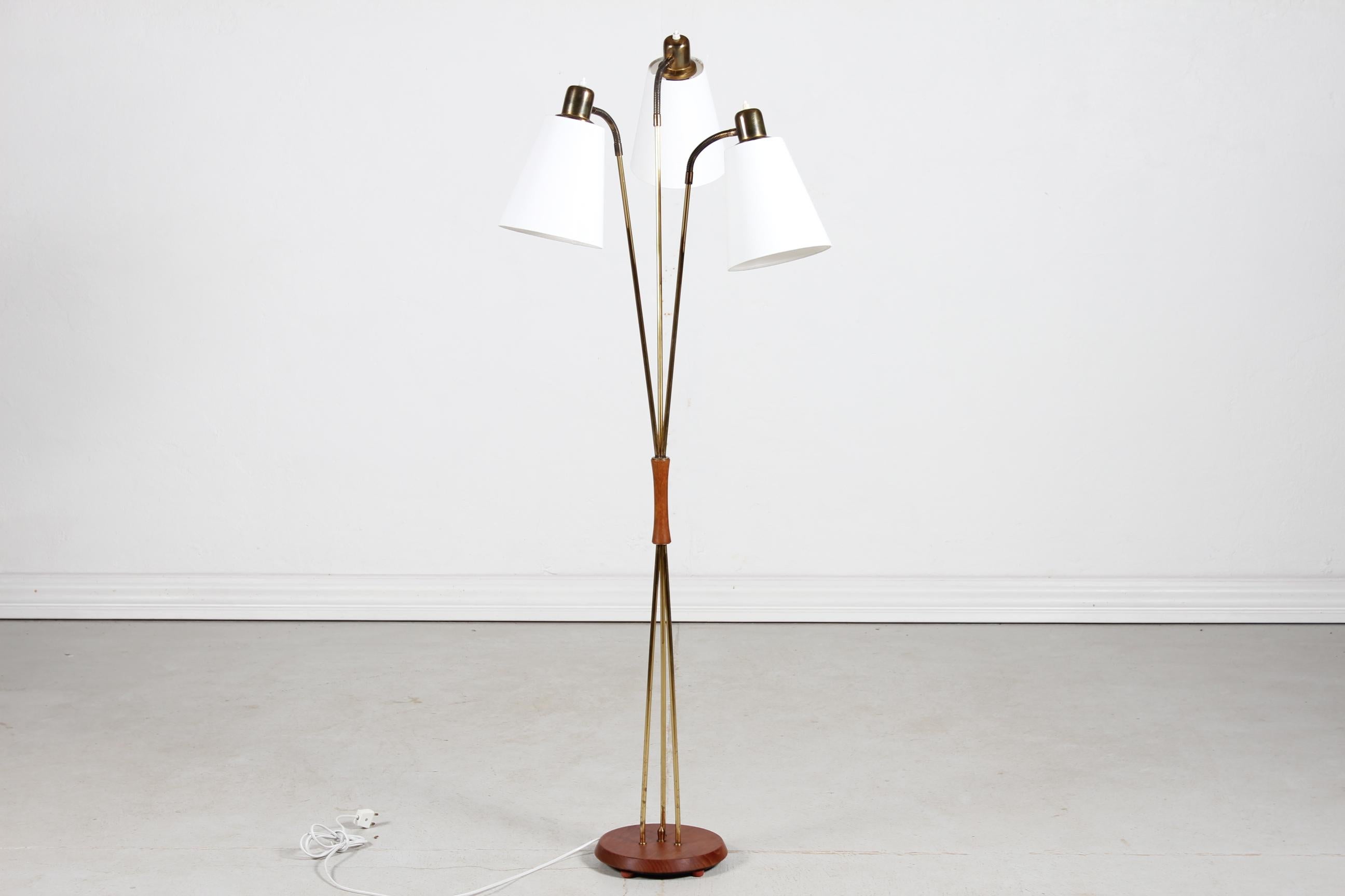 Scandinavian modern three-armed floor lamp made of brass with patina. 
The base and middle piece of the stem is made of teak. 
All three arms are individually adjustable and possible to turn on and off one by one. 
Mounted with new shades.

The