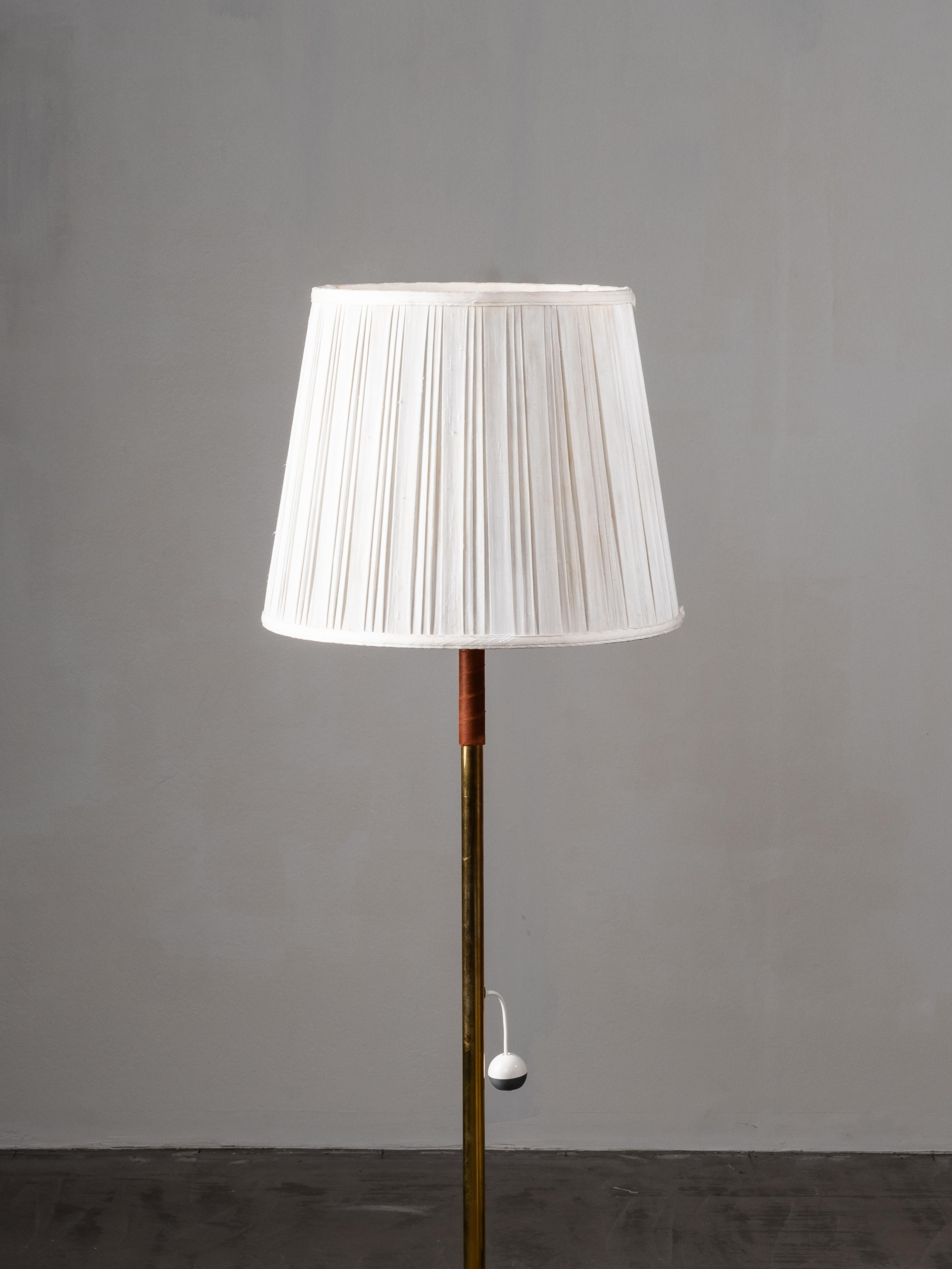 Elegante lampada da terra scandinava Mid-Century Modern realizzata in ottone con proporzioni raffinate e semplicità senza tempo. L'elegante gambo in ottone è accentuato da un dettaglio in pelle avvolto a mano, che aggiunge calore e contrasto tattile