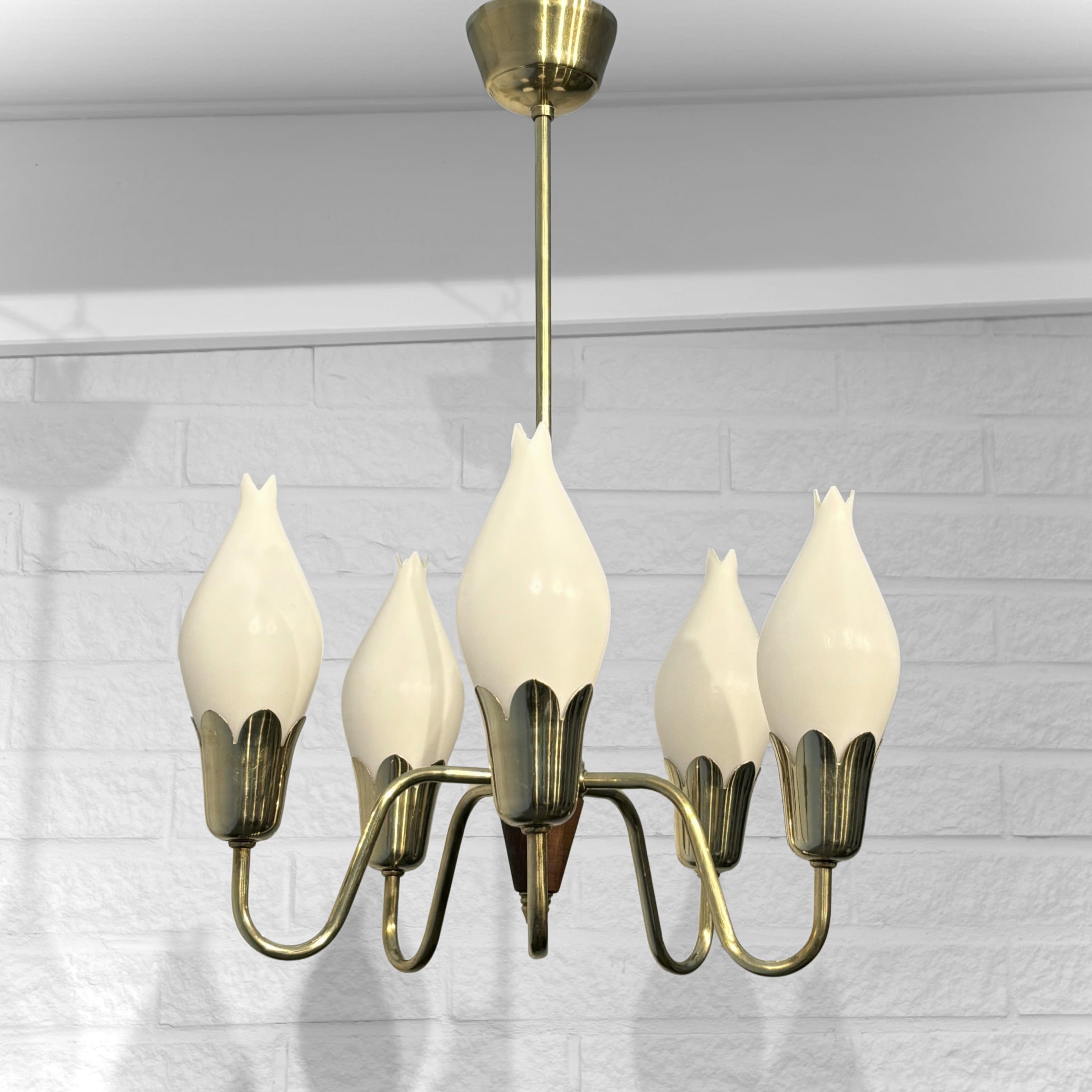 Un lampadario moderno di metà secolo attribuito al produttore danese Fog & Mørup, risalente agli anni Cinquanta. Questo elegante pezzo è realizzato in ottone e presenta cinque bracci, ognuno dei quali sostiene un paralume in vetro opalino a forma di