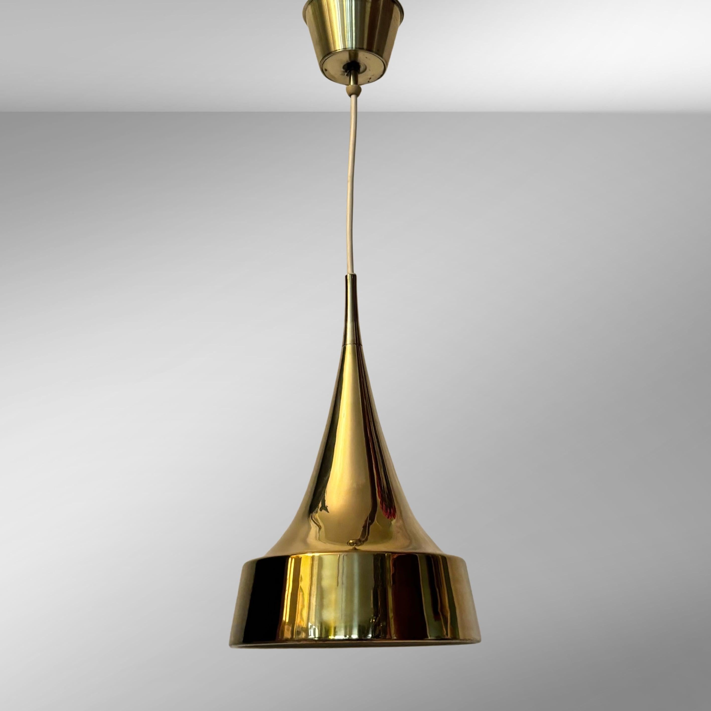 A minimalist pendant lamp designed by Eje Ahlgren for the Swedish lighting manufacturer Bergboms in the 1960s. Constructed from a cone shaped brass shade, a brass canopy up by the ceiling and a white plastic wire.

The Swedish designer Eje Ahlgren