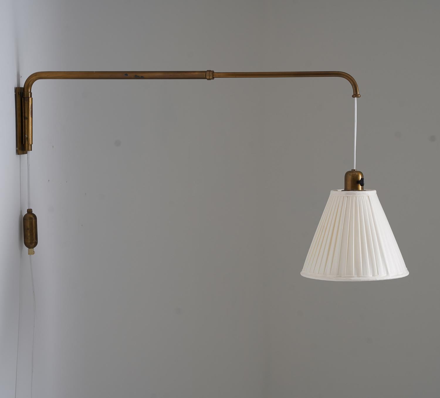 Elegant wall-mounted lamp manufactured in Sweden during the 1940s. Made from patinated brass, it features a telescopic arm with a classic swing design, allowing the light source to be extended or retracted smoothly. The shade height is easily