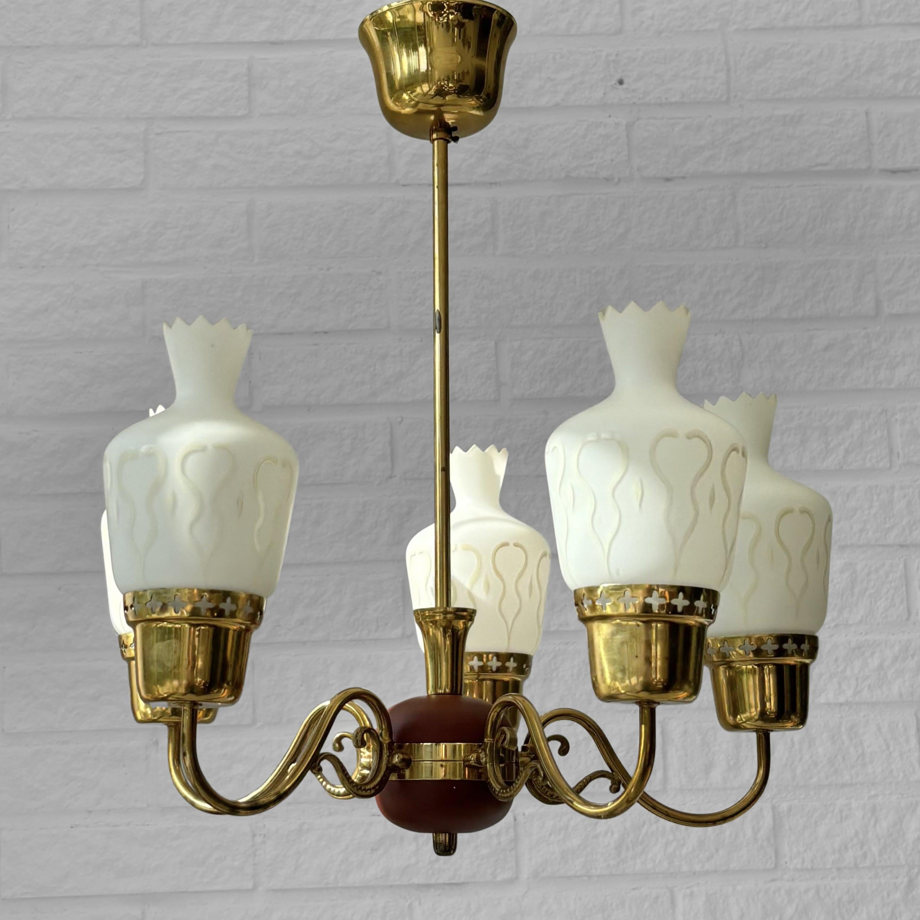 Lampadario scandinavo della metà del secolo scorso, prodotto da un produttore svedese non identificato negli anni '50. Realizzato in ottone, presenta cinque bracci decorativi che si estendono da un elemento centrale in legno, ognuno dei quali