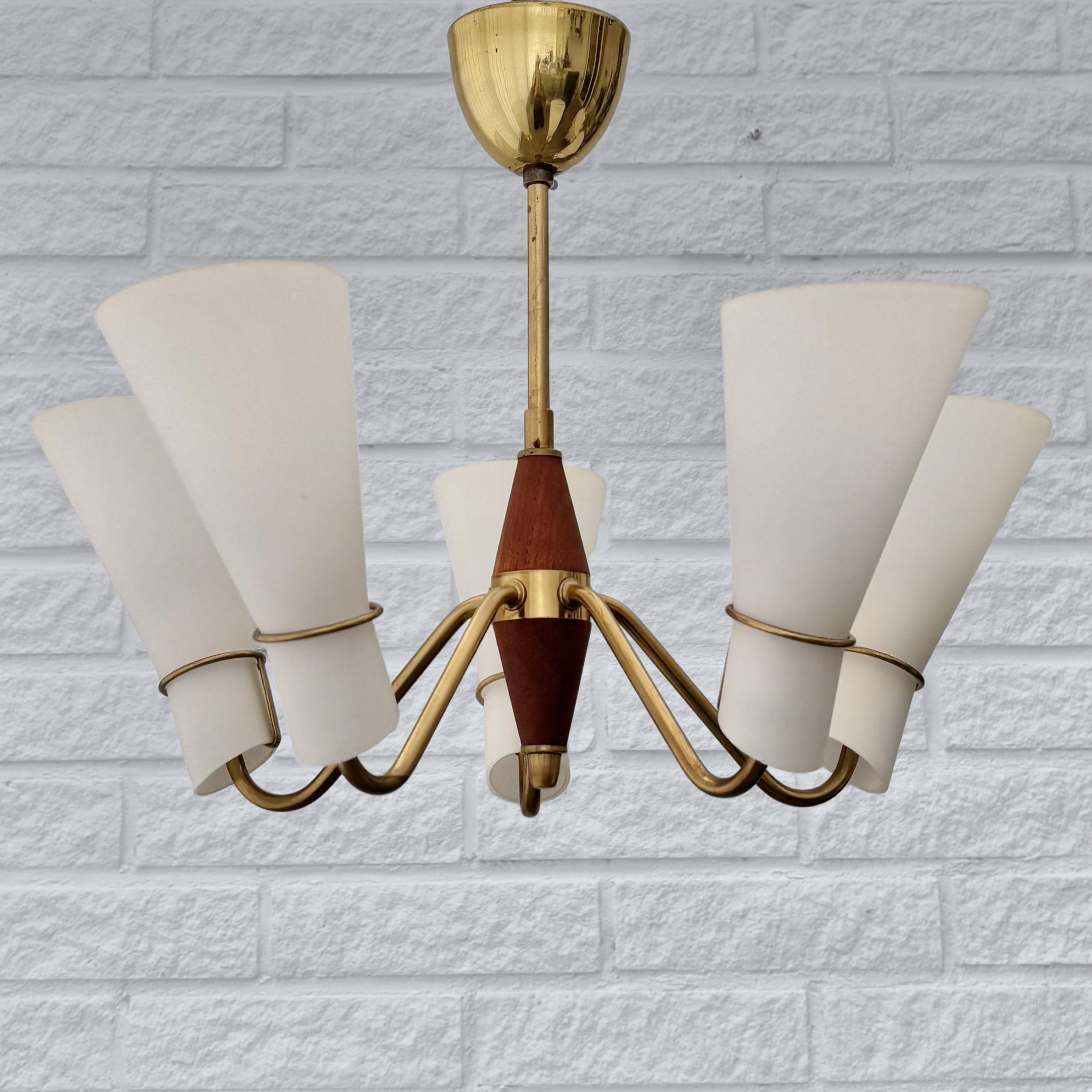 Un bellissimo lampadario scandinavo di metà secolo, realizzato in ottone con dettagli in teak e dotato di cinque paralumi scultorei a forma di cono in vetro opalino. L'apparecchio è sospeso a un pilastro in ottone e viene fornito con il suo