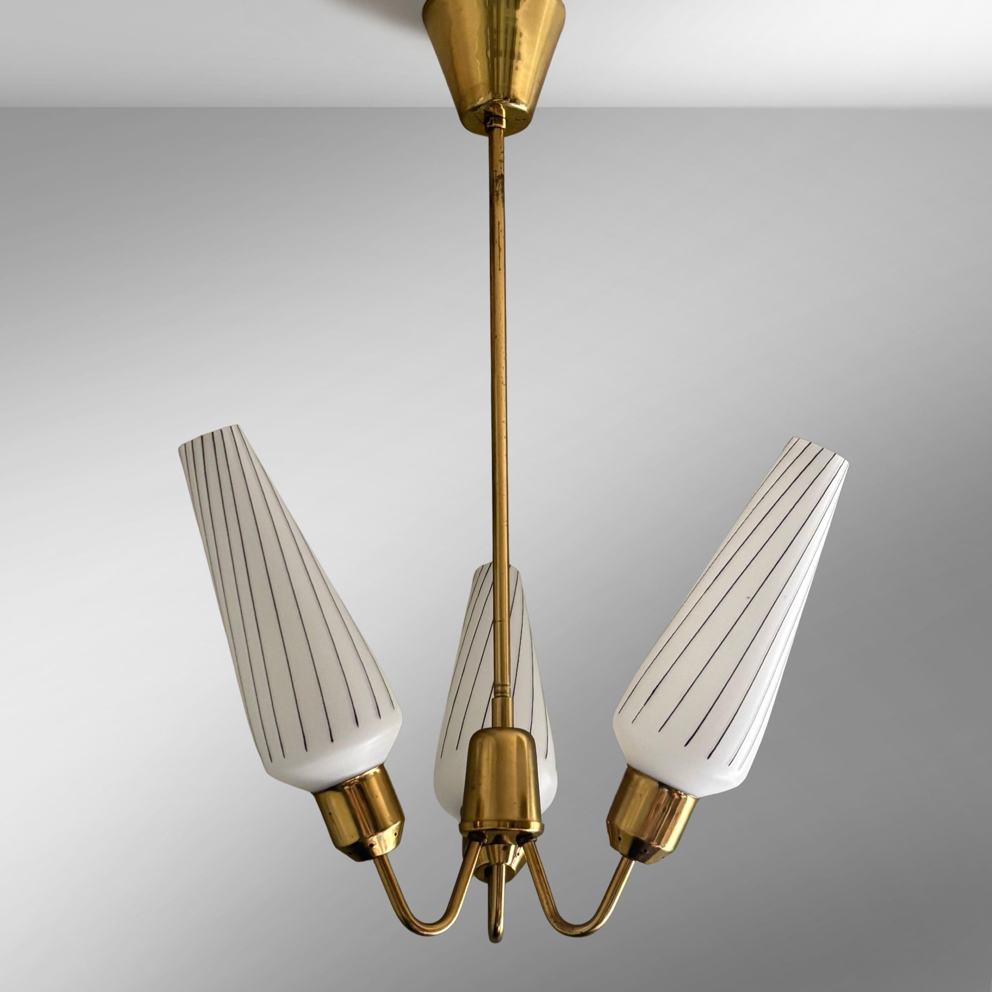 Scandinavian mid-century pendant lamp, produced by an unidentified Swedish manufacturer in the 1950s. Crafted from brass, it features three curved arms attached to a bell-shaped centerpiece, each holding a cone-shaped glass shade with geometric