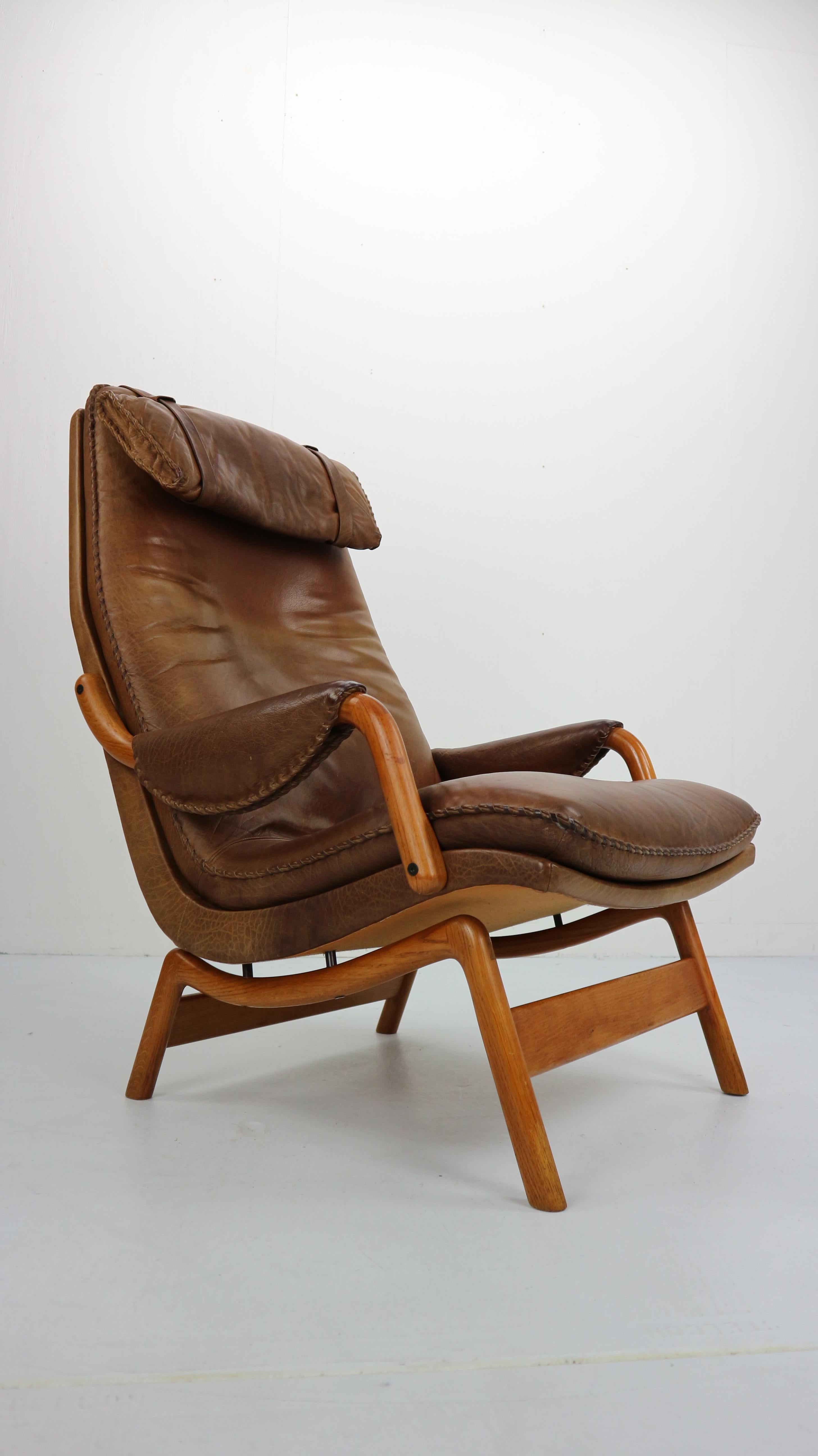 Beautifully streamlined, unique and special Scandinavian leather lounge armchairs. 
The chair has an headrest and elegant curved oak legs. 
Made in 1960s.