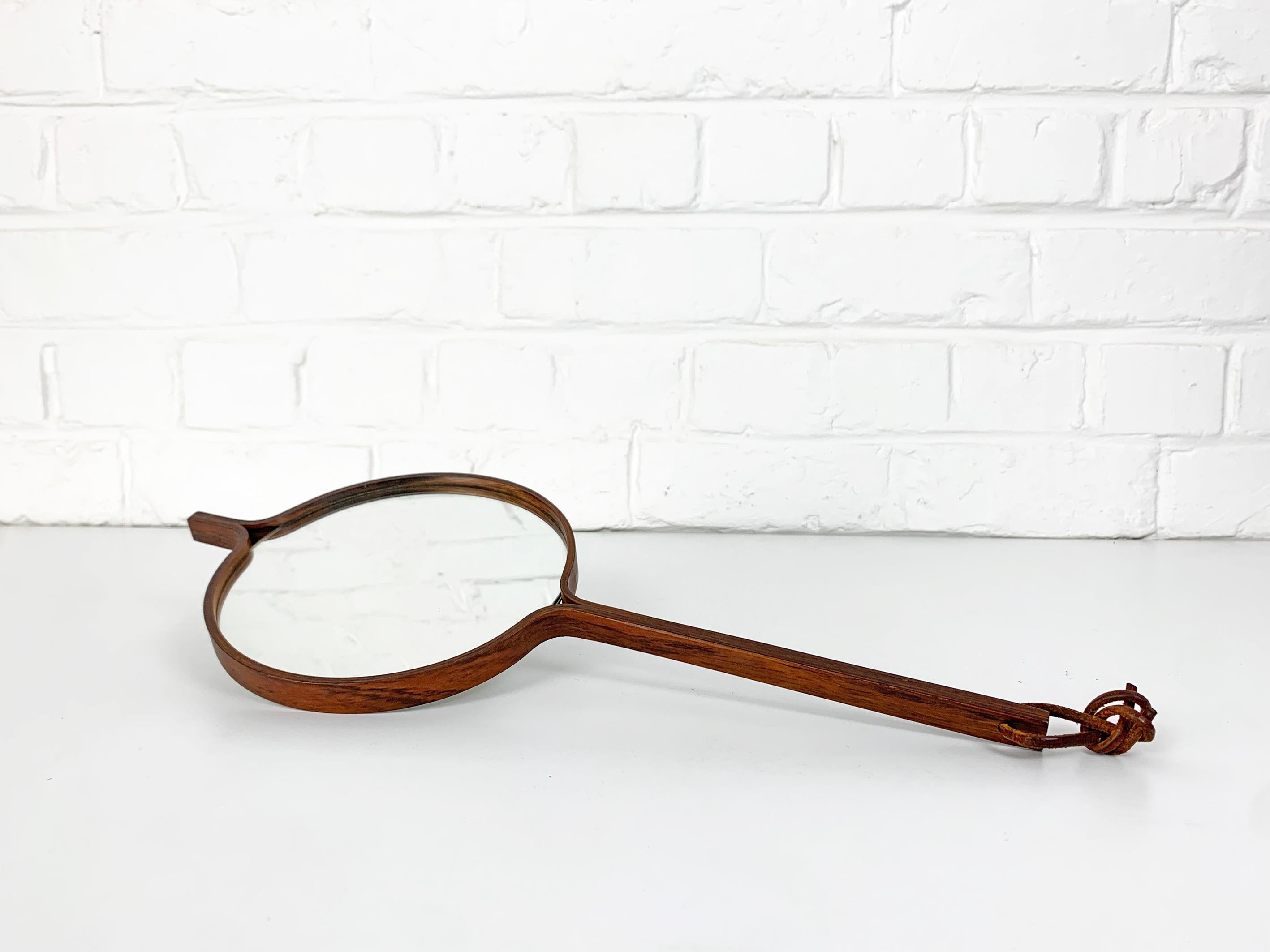 Mid-Century Hand mirror in ebonized wood or teak wood by Bech & Starup for Den Permanente, Denmark. Scandinavian minimalistic design.

Features a leather strap for wall hanging, can be used as a wall- or hand-mirror. 

This mirror has often be