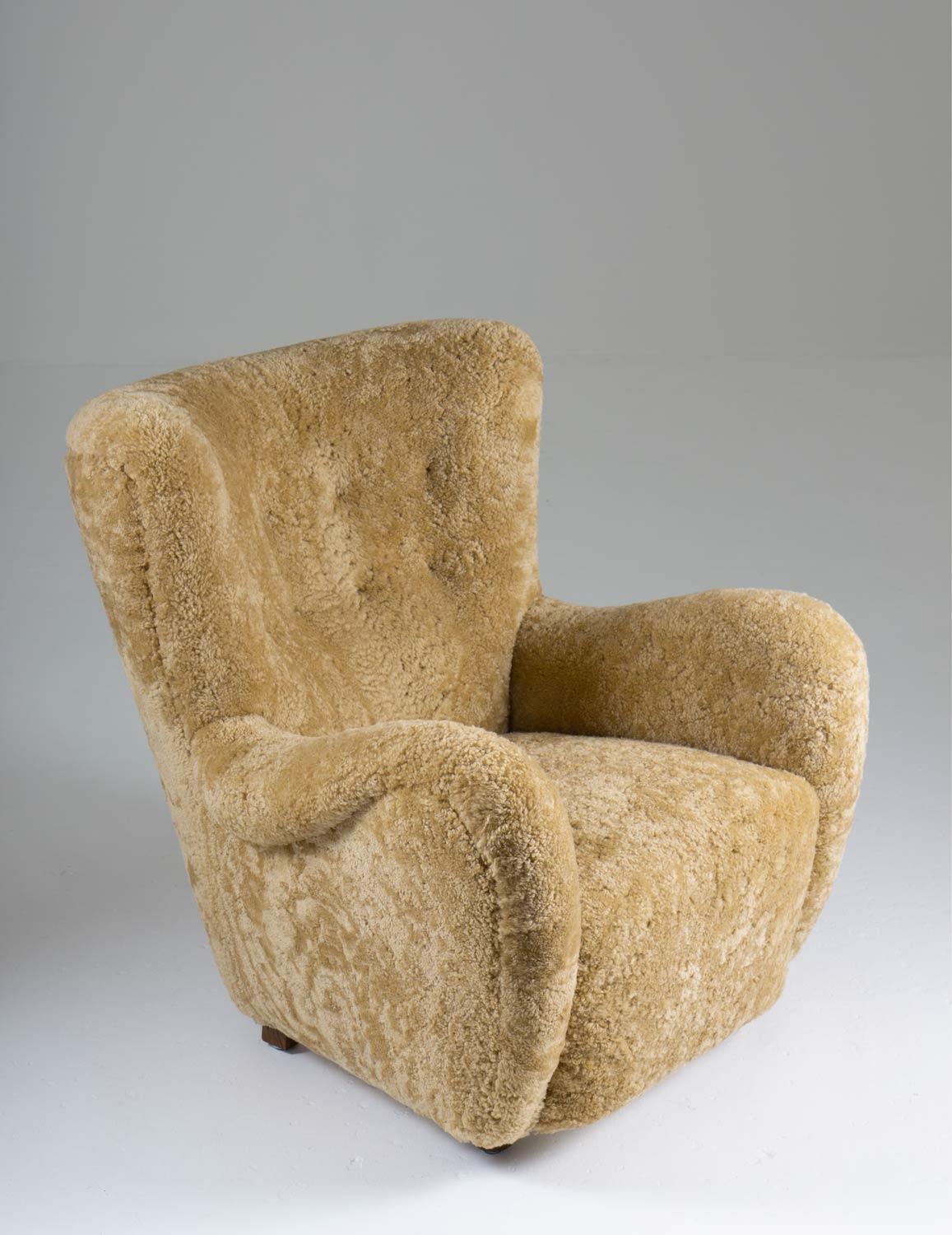 High-back lounge chair manufactured in Denmark ca 1940. 

This majestic chair surrounds you with its curved backrest and is just as comfortable as it looks. 
It's been reupholstered in honey-colored sheepskin and cognac leather