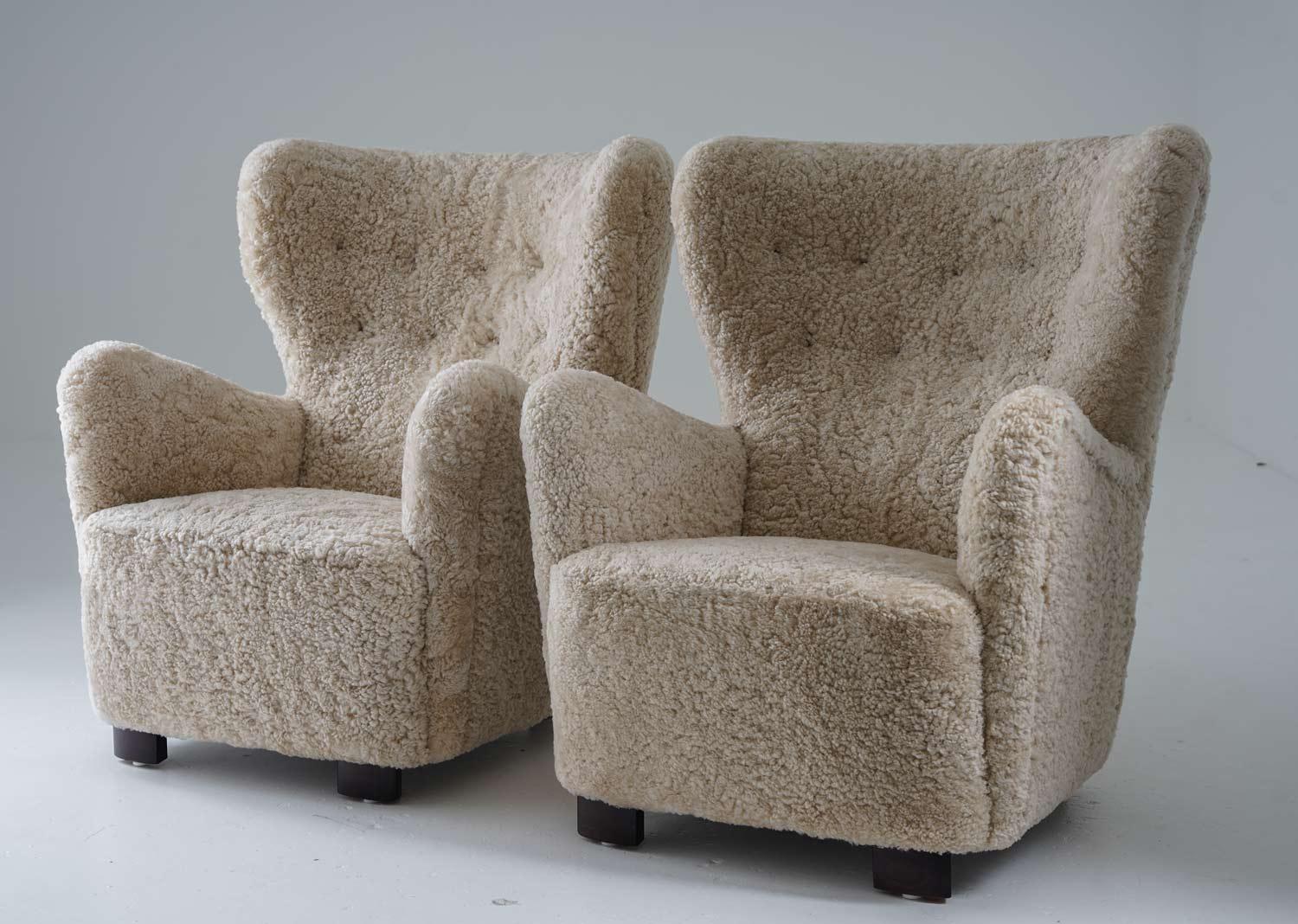 Pair of large high-back lounge chairs manufactured in Denmark, 1930s. 
These majestic chairs surround you with their curved backrest and are just as comfortable as they look. 
They've been reupholstered in honey-colored sheepskin and cognac