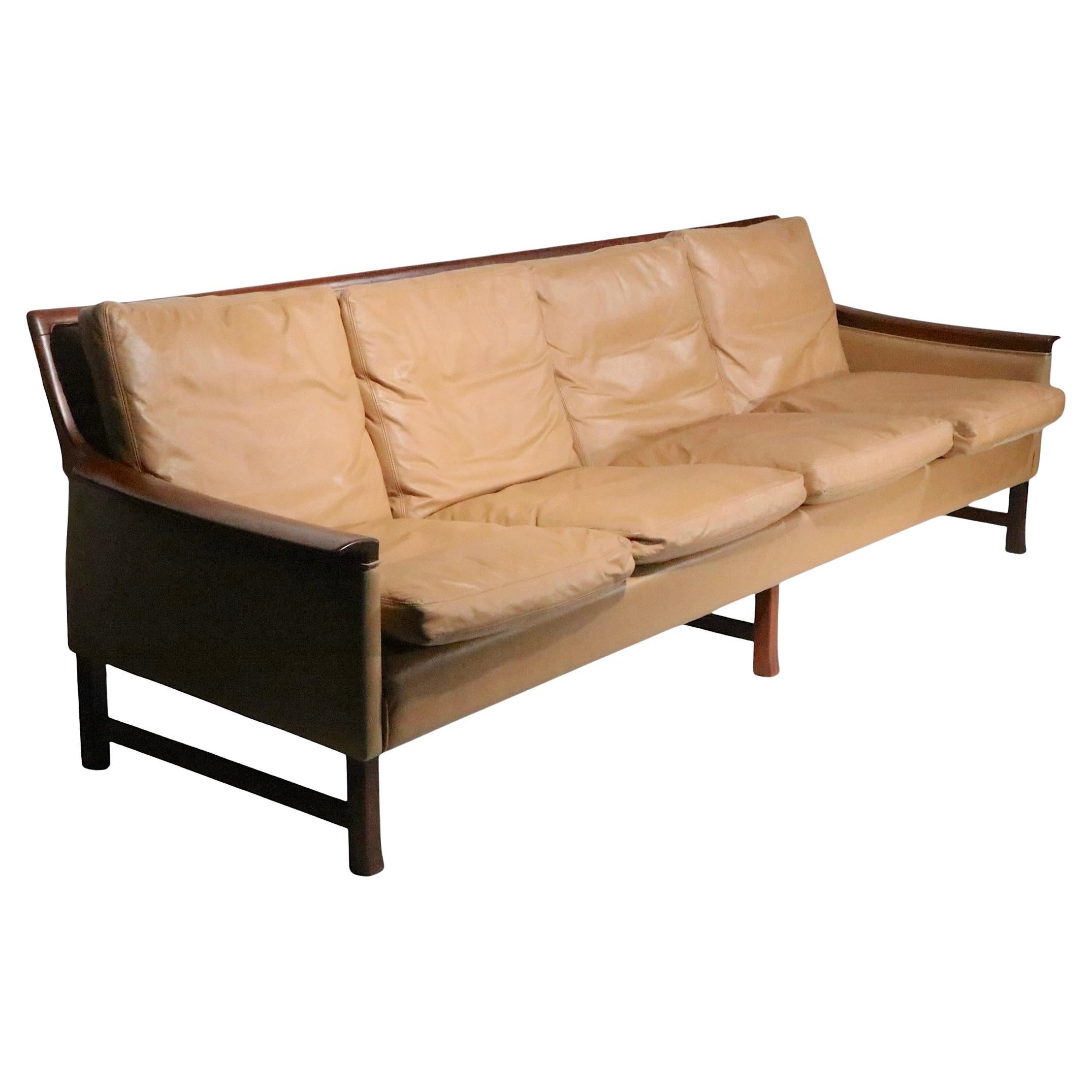 Exceptional Scandinavian Mid Century Modern leather and rosewood sofa, in very clean, original, ready to use condition. The sofa features rich leather loose fitting seat and back rests, with elegant sculptural rosewood arm rests.   This piece is