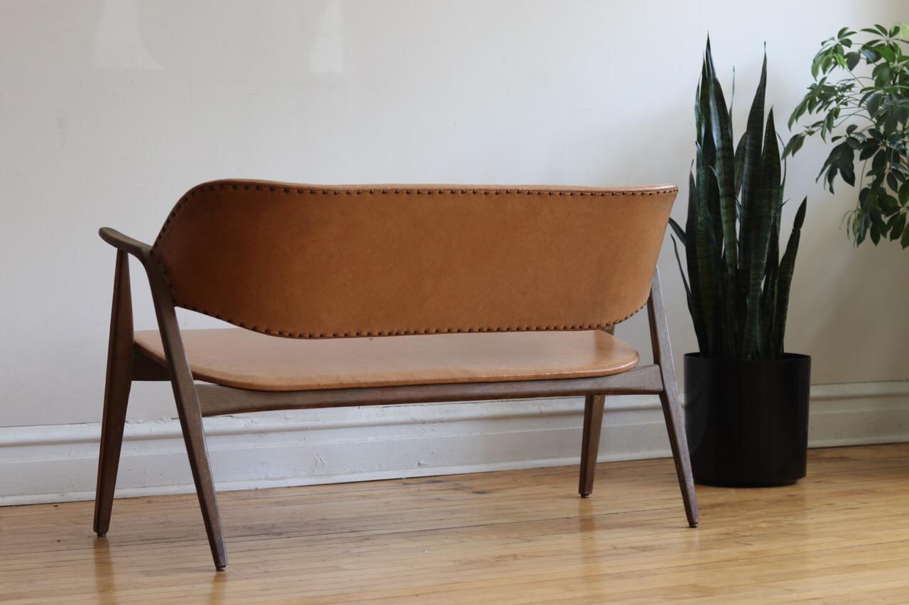 Early Mid-Century Modern Danish settee bench.
Curved wooden back.
Studded leather.
Light peach-beige-tan leather.
In original vintage condition.
Wood and leather worn. 
Some small tears in the leather.
Measures: 48 1/4