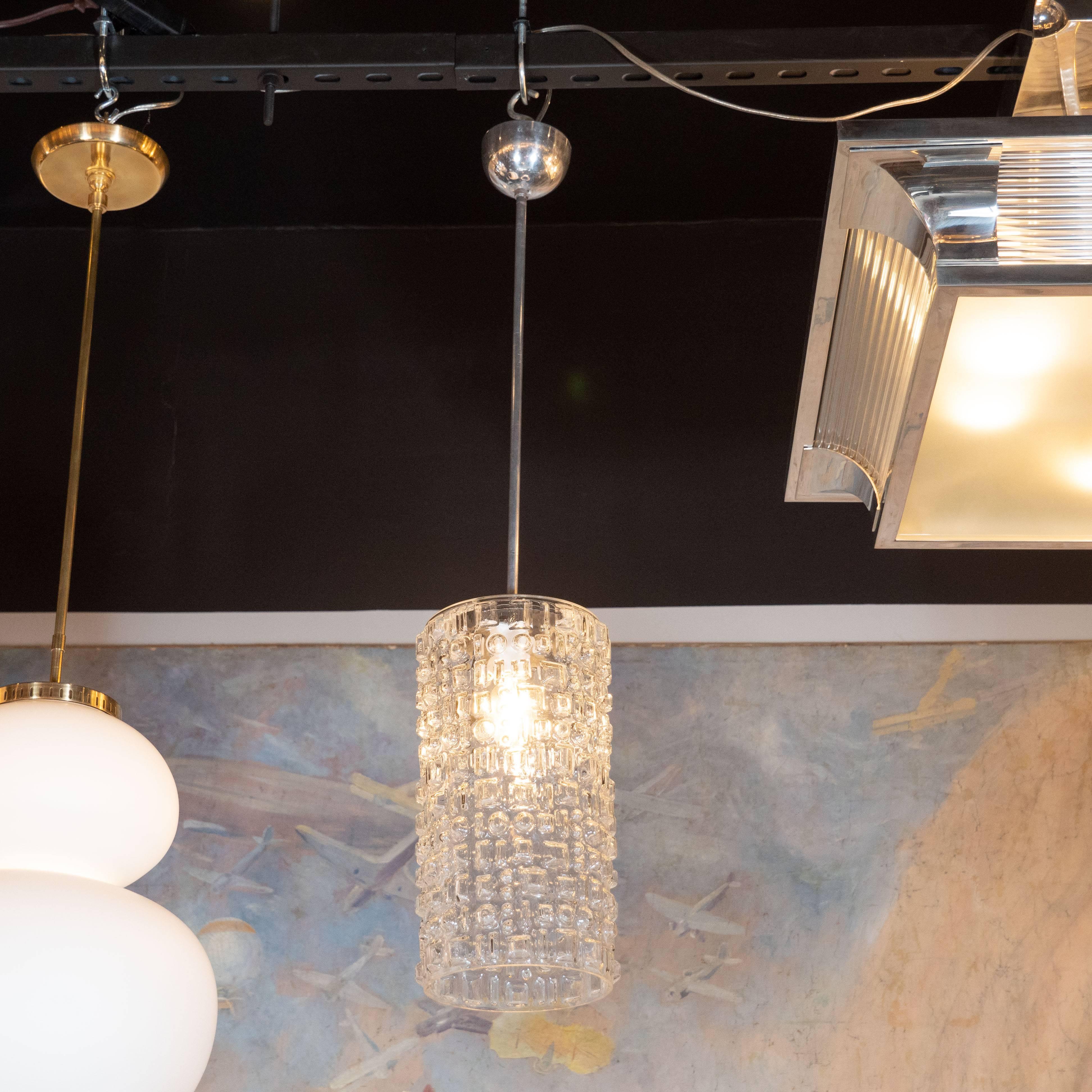 This refined and understated pendant was realized in Sweden, circa 1960. It offers a cylindrical body in molded highly textural glass with an abundance of protuberant geometric forms in relief on the surface. The fixture connects to the ceiling via