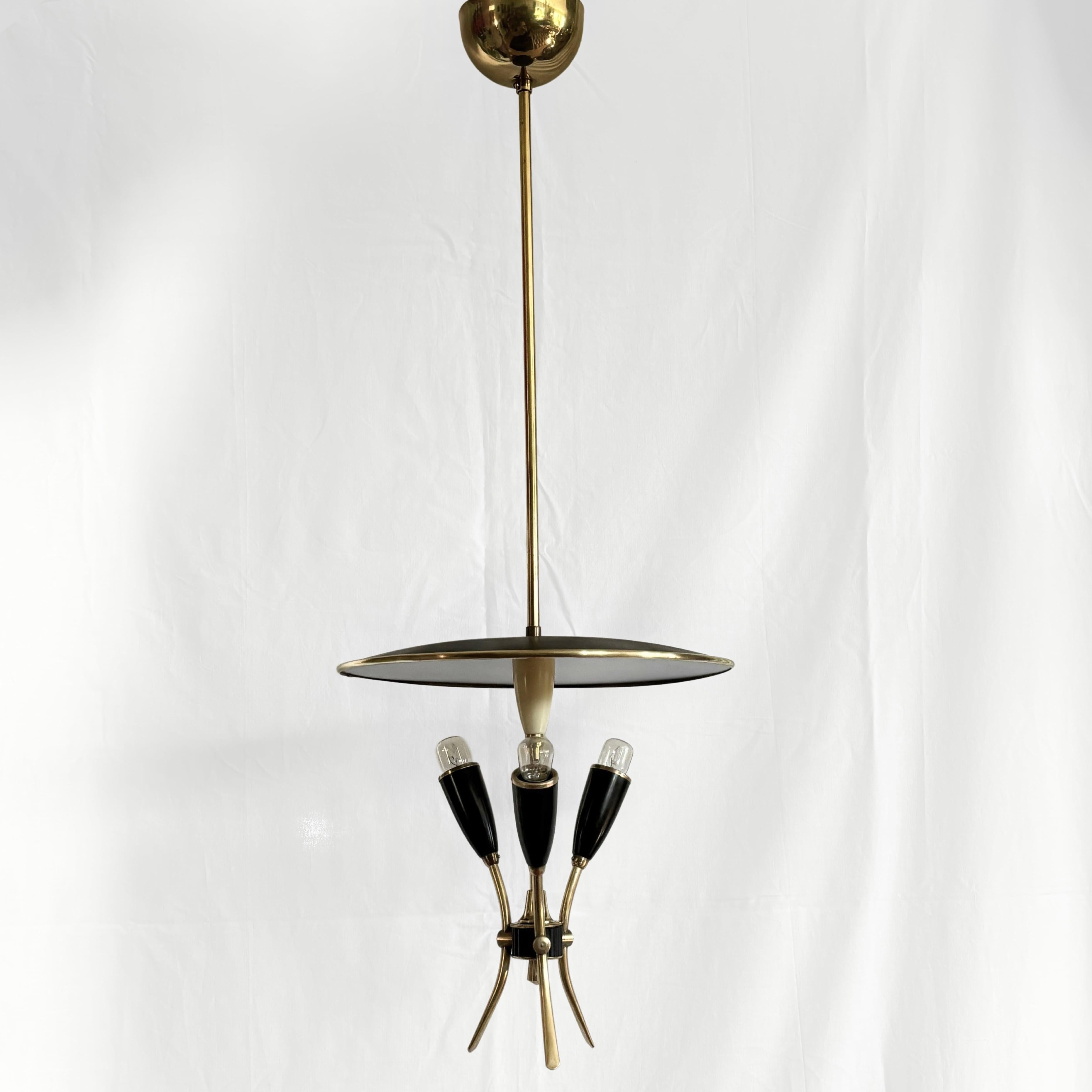 Un apparecchio a sospensione futuristico e spaziale prodotto da un fabbricante svedese non identificato negli anni '60. Presenta un riflettore metallico a forma di disco e tre portalampada neri, tutti tenuti insieme da una struttura in ottone.