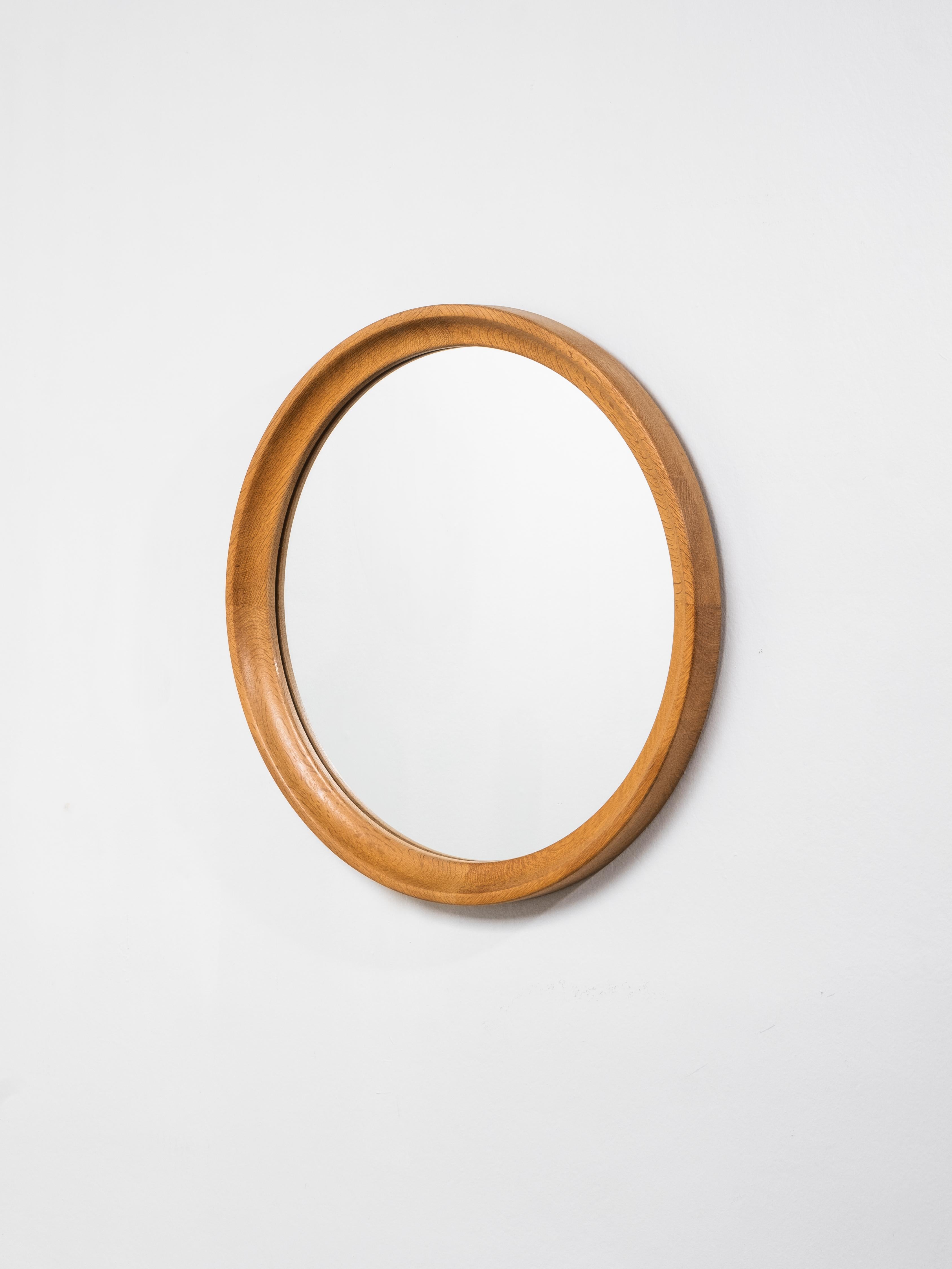 A finely crafted Scandinavian mid-century wall mirror featuring a sculpted solid oak frame with a soft, rounded profile. The frame’s deep bevel and continuous curve highlight the natural grain and warmth of the oak, reflecting the timeless Nordic