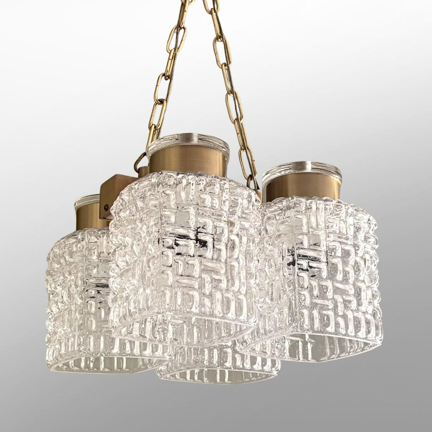 Lampada a sospensione modernista scandinava attribuita a Carl Fagerlund per la vetreria svedese Orrefors. Realizzato in ottone, presenta quattro paralumi in vetro ornati da un motivo organico in rilievo. L'apparecchio è sospeso a due catene di