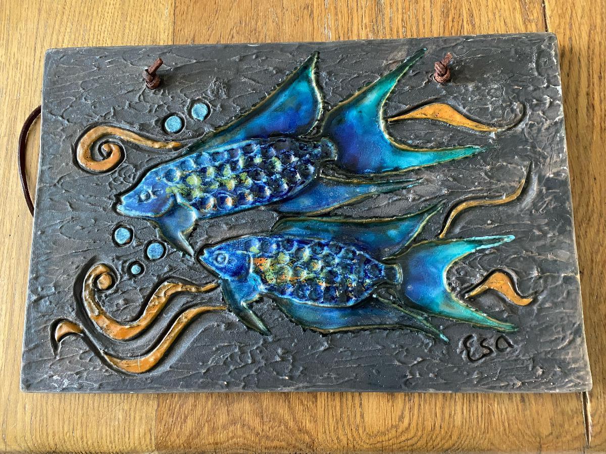 Nice stoneware wall plaque relief of two fishes in bright colors by Tilgmans Pottery Sweden. The plaque has a leather strap for hanging on the wall.

At the front there are the initials of the maker engraved and on the bottom the wall plaque is